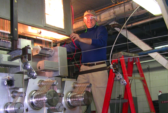 S. Edward Law smiles while wearing safety goggles atop a ladder while working with large machinery