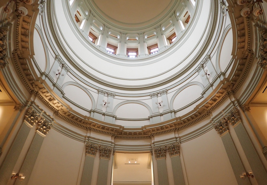 Looking up at the inside of the dome of the Georgia capitol building with white walls and detailed scaffolding with warm sconce lights.