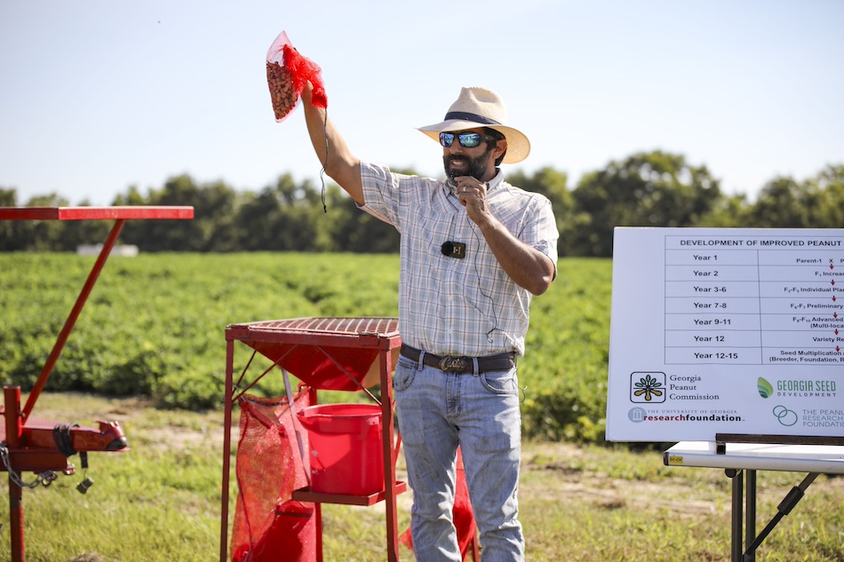 Nino Brown stands in front of a peanut field holding up a red net bag of harvested peanuts above his head as he speaks to participants in the Georgia Peanut Tour in 2022. . 