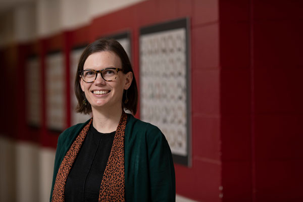 A woman with shoulder-length brown hair, glasses a black shirt and an orange cheetah print scarf smiles at the camera