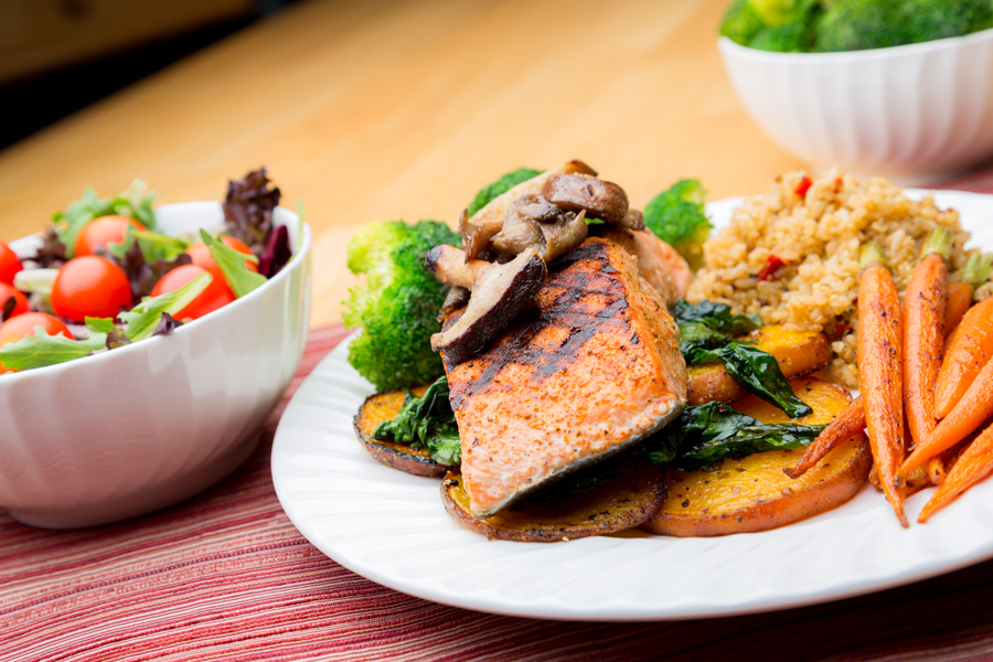 A healthy meal of salmon, vegetables, rice and a salad plated on a table.