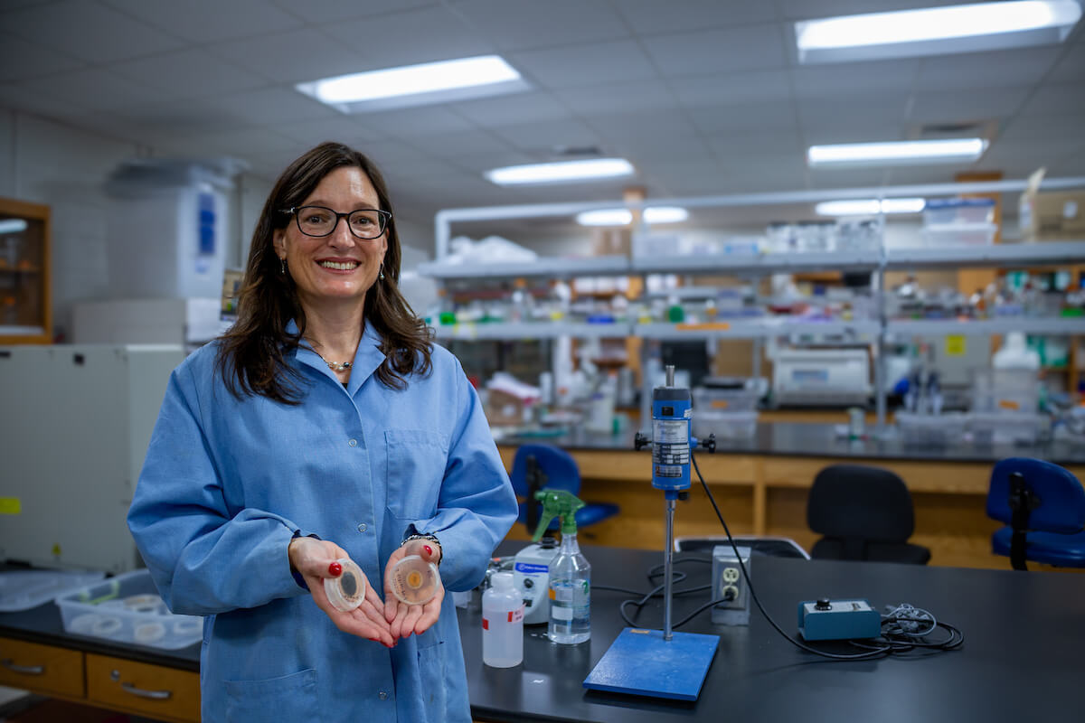 Marin Brewer holds Petri dishes while wearing a blue lab coat in her lab