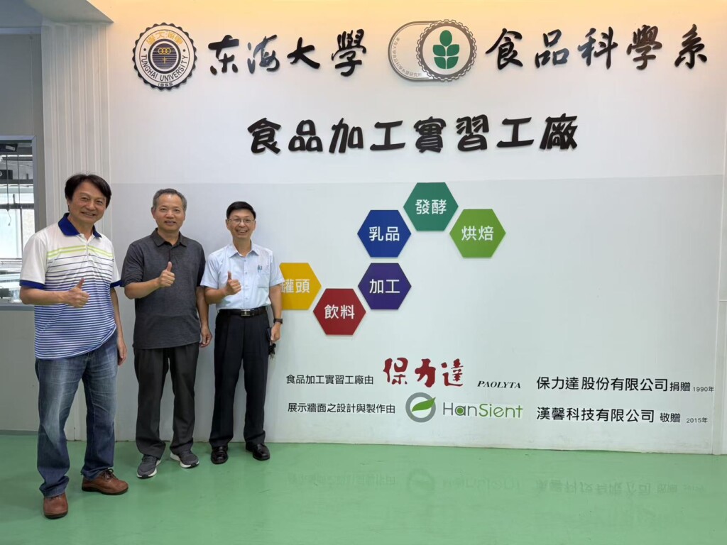 Three men give thumbs-up gestures in front of a display at Tunghai University.