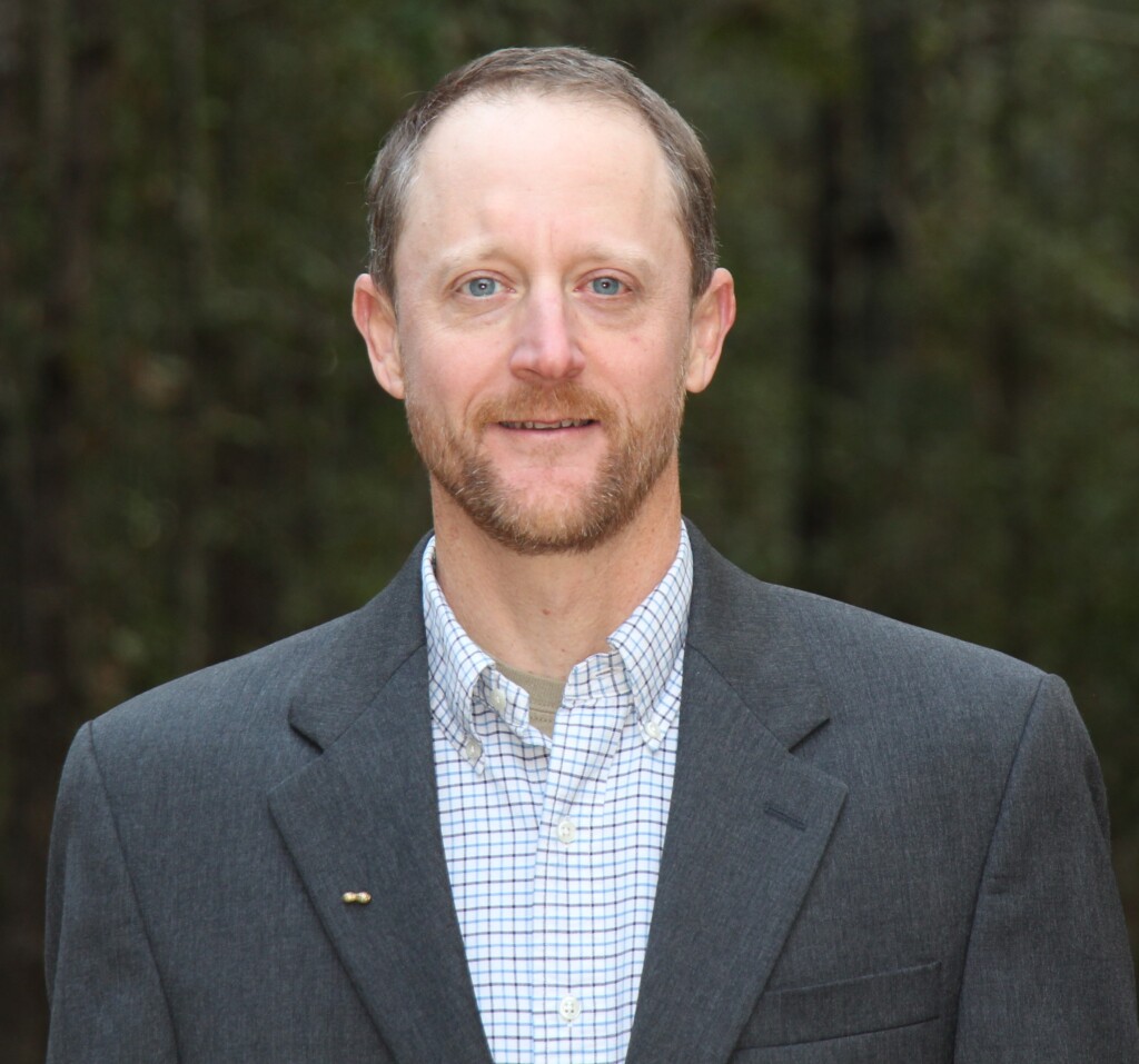 Mark Abney smiles while wearing a suit
