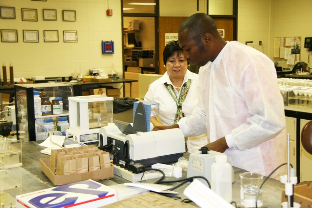 a man and a woman in a laboratory setting working with a piece of equipment on the lab bench