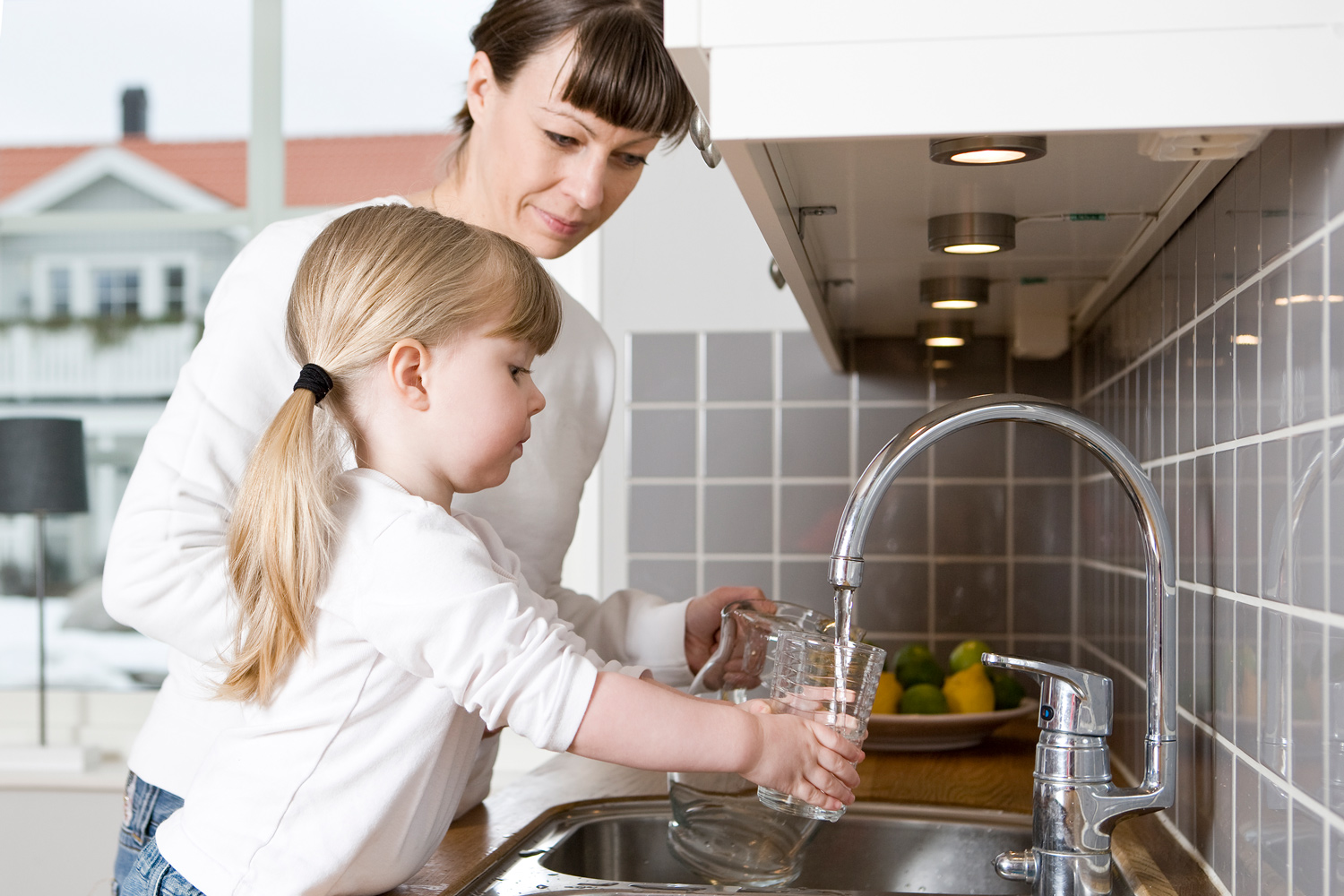 A woman and a young girl get water from a kitchen faucet