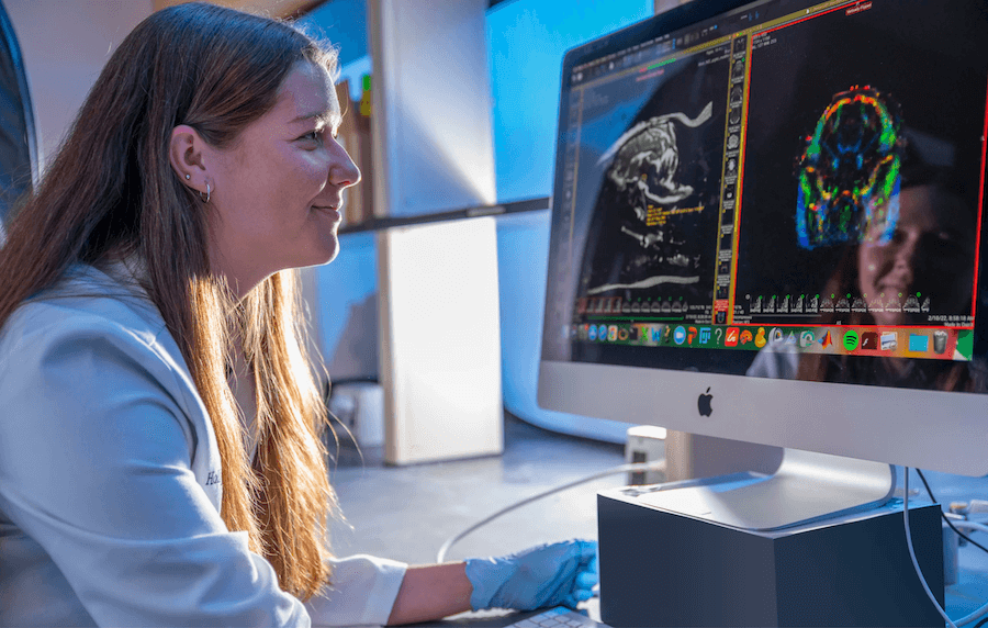 A woman in a lab coat looks at scans on a computer screen.