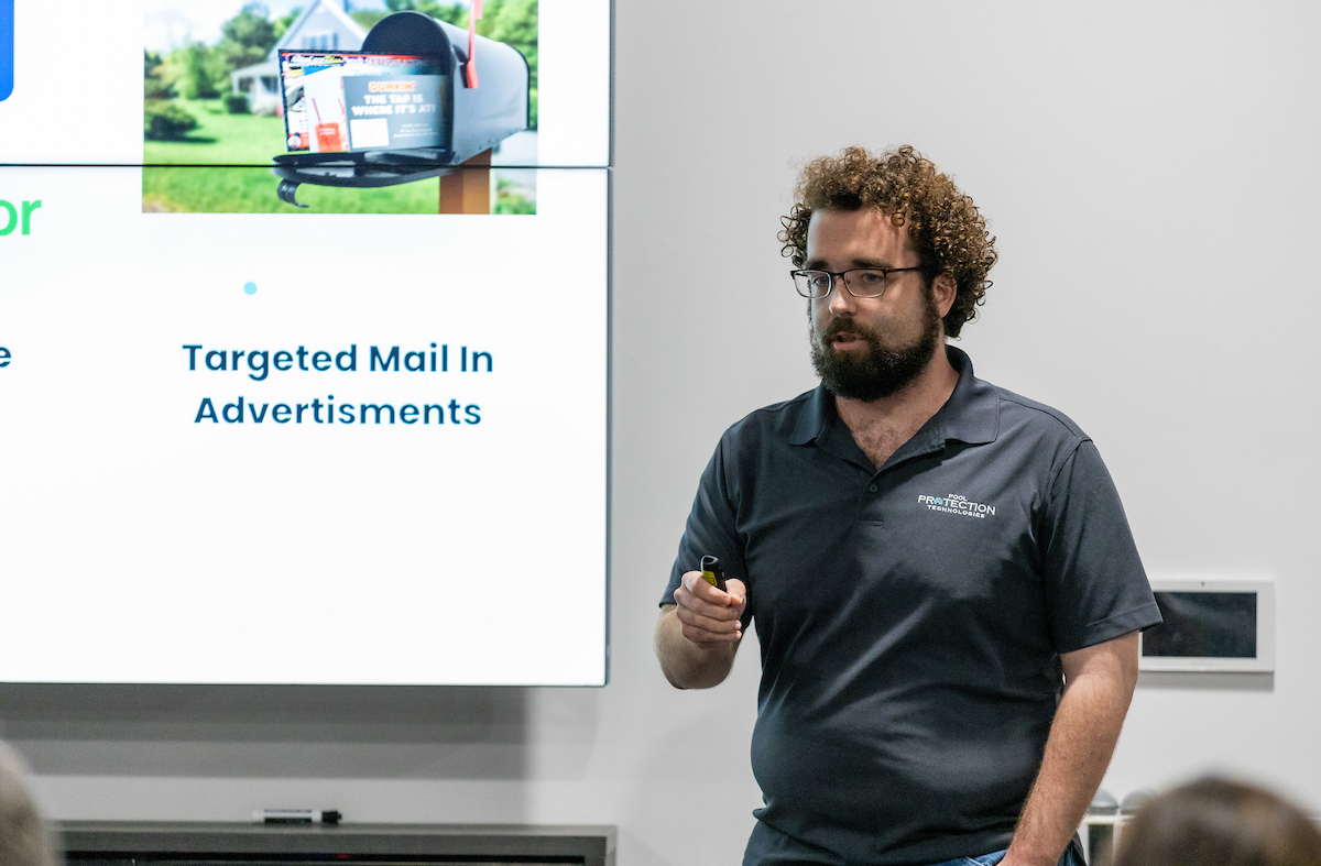 A man with curly hair and a beard presents at a pitch contest.