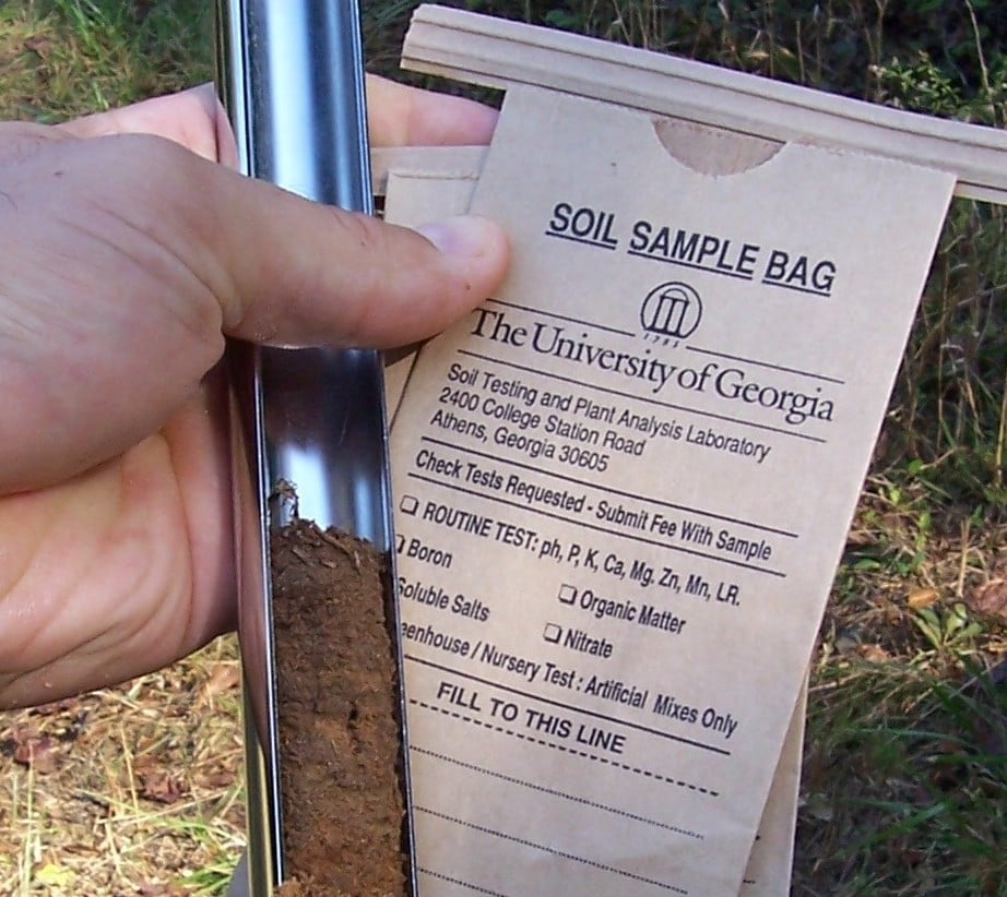 a hand holds a tool for collecting soil and a soil sample bag from UGA