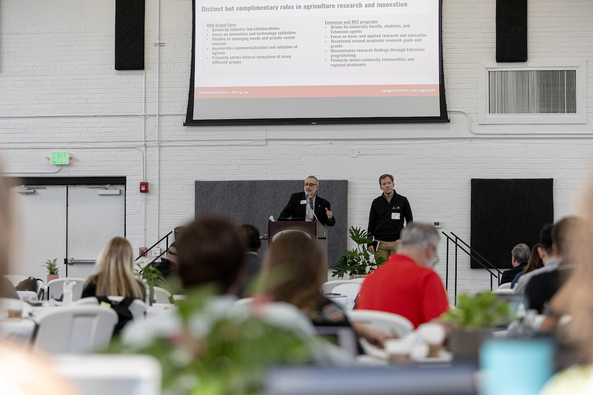 Two men stand on a stage in front of a crowd during a conference.