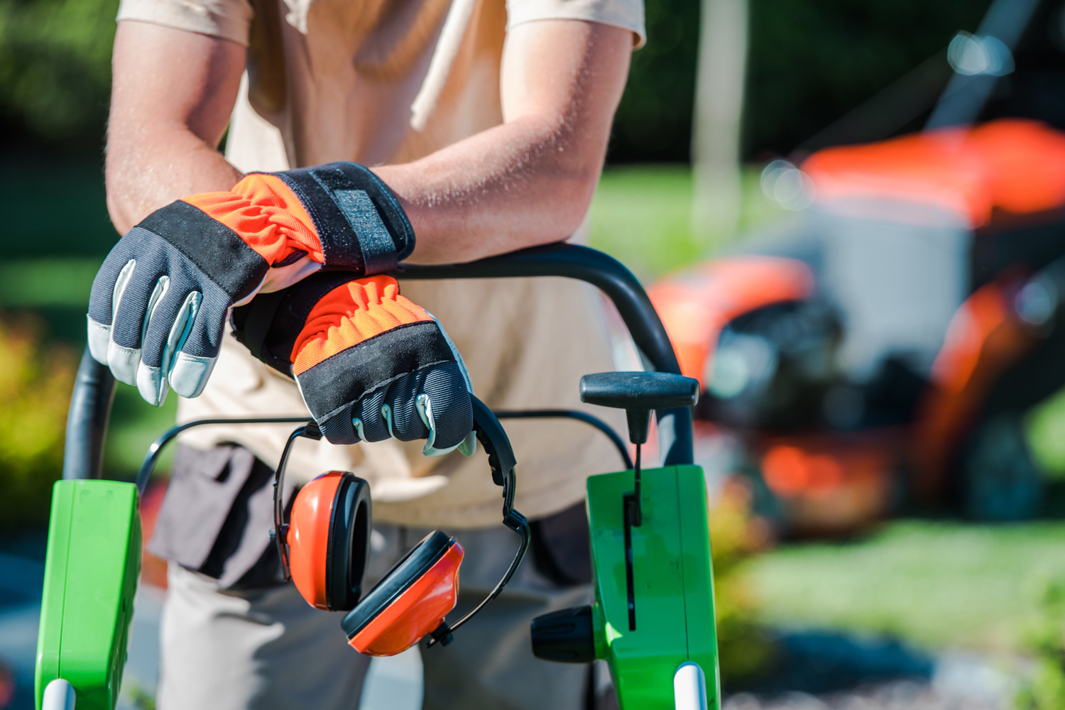 a landscaper wears gloves and holds hearing protection while getting ready to work