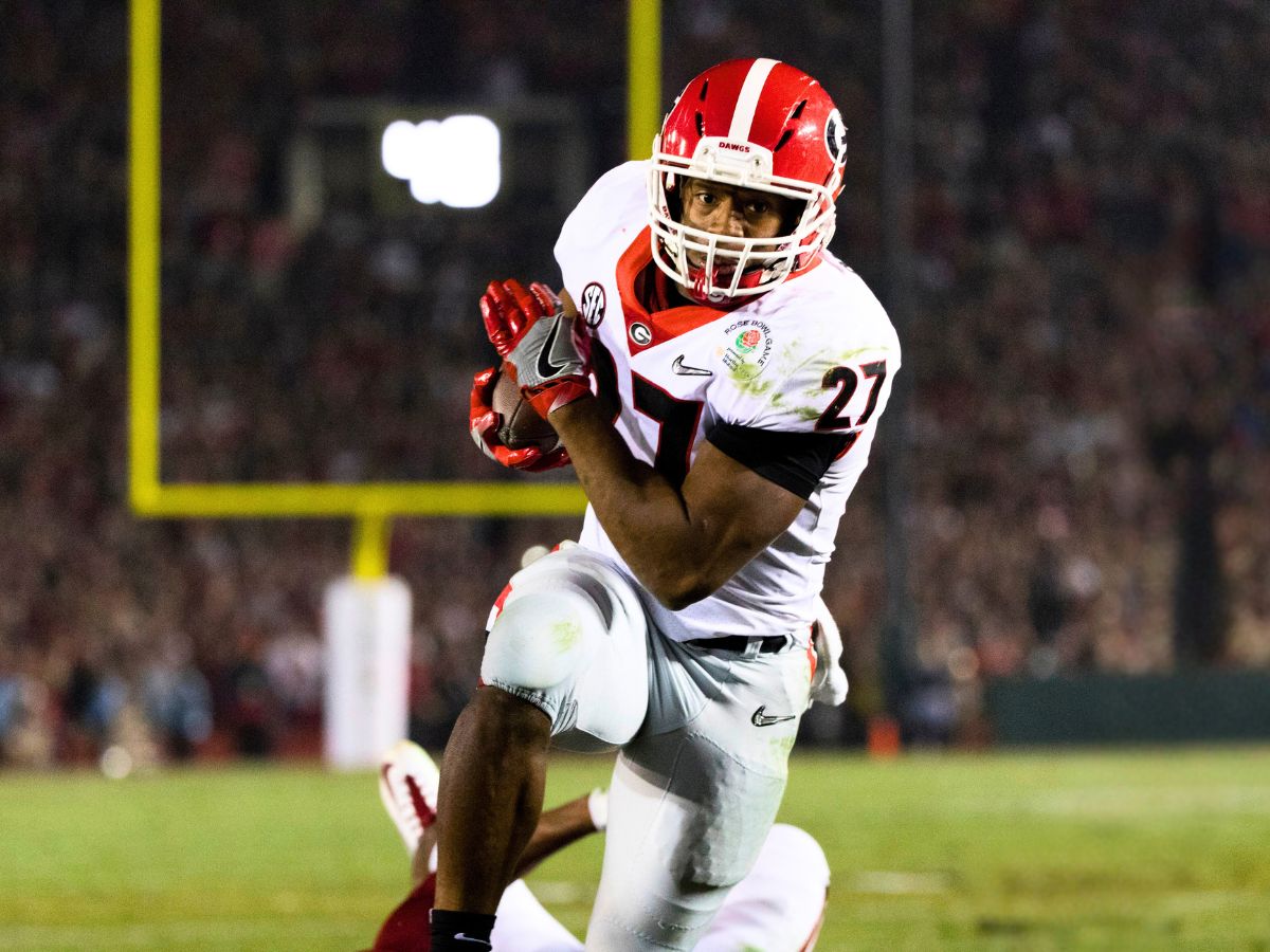 A football player holding a football during a game and running towards the camera.