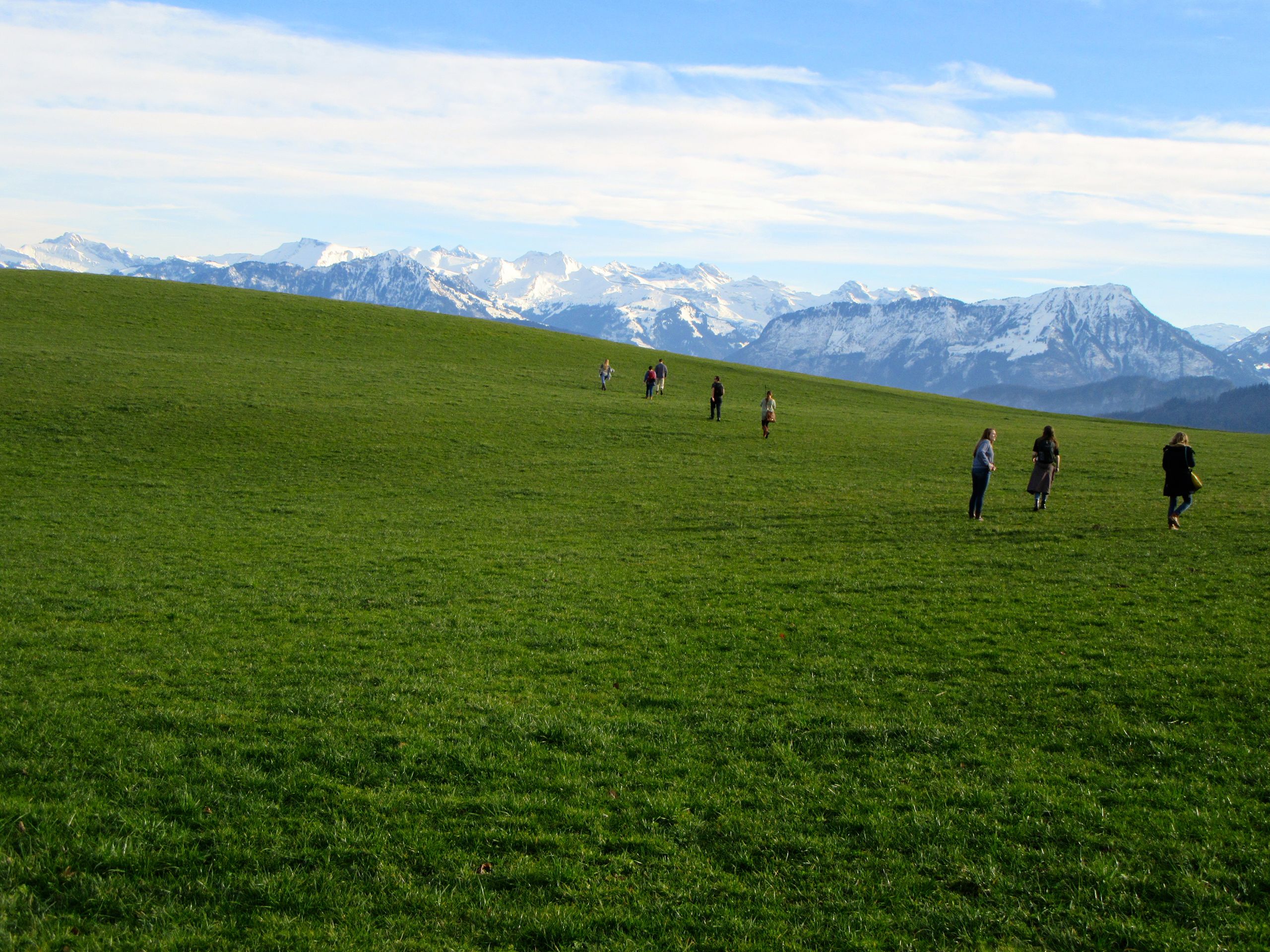 People stand on a grassy hill with mountains in the background.