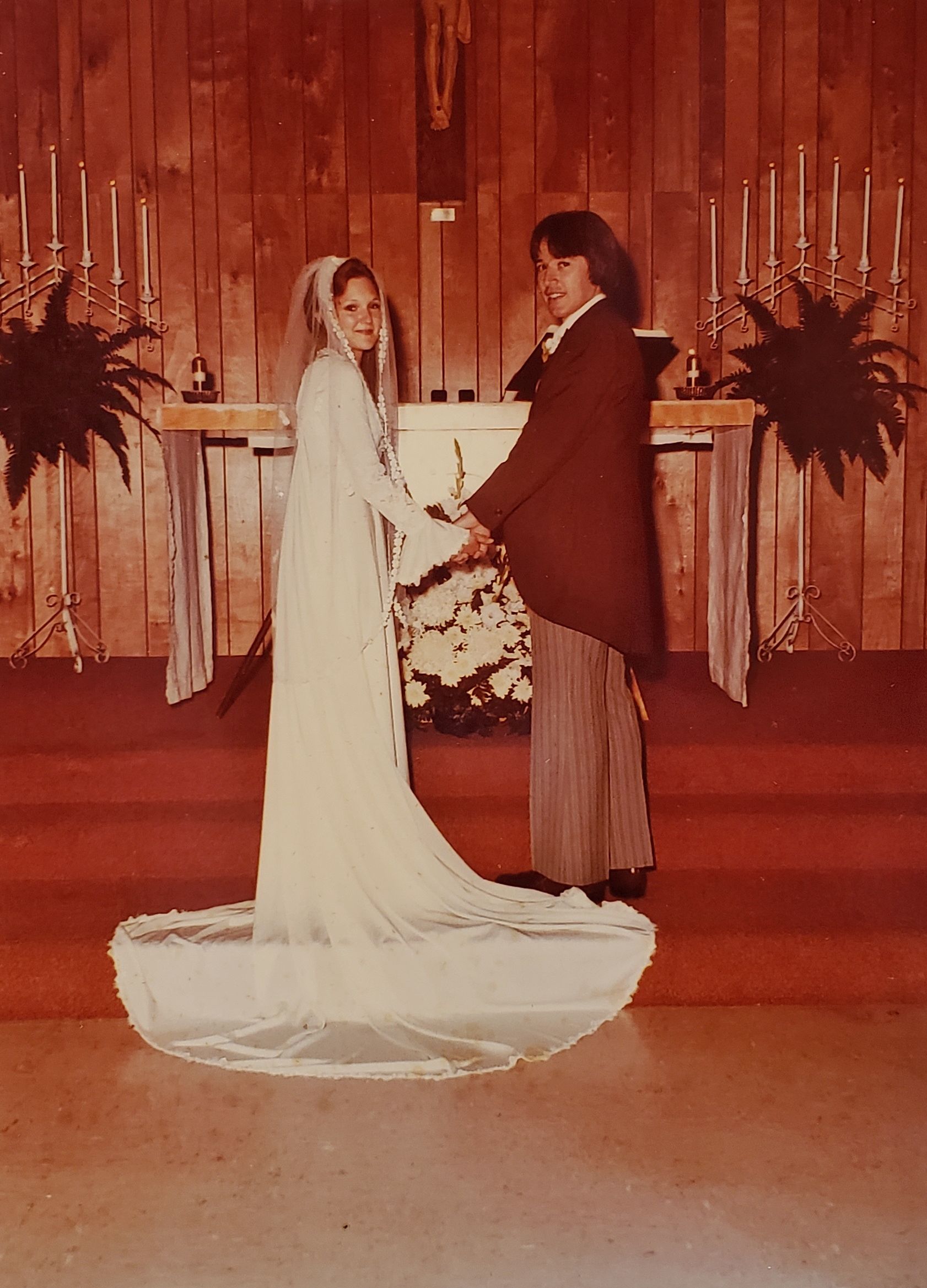 Wedding photo of Joe Broder and Diane Brownlee holding hands in front of a fireplace