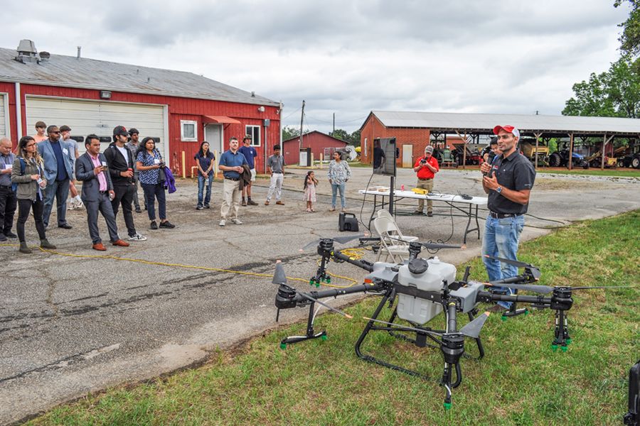Professor Simer Virk stands next to a spray drone, presenting to IPA conference attendees