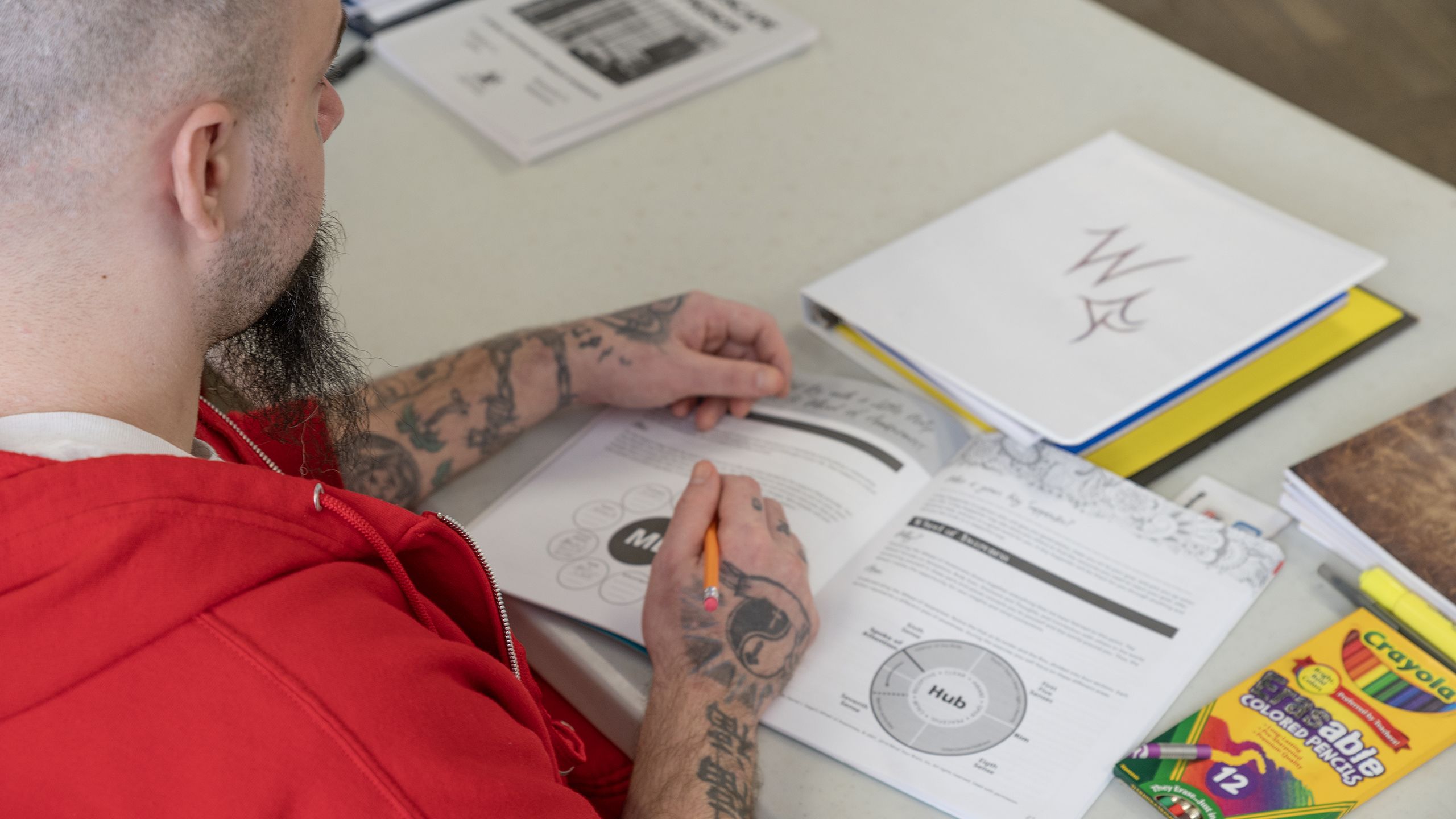 A participant engages with a "Mind Matters" workbook during a session led by Extension Agent Georganne Cooke, focusing on a page with drawings and text annotations in a classroom setting.