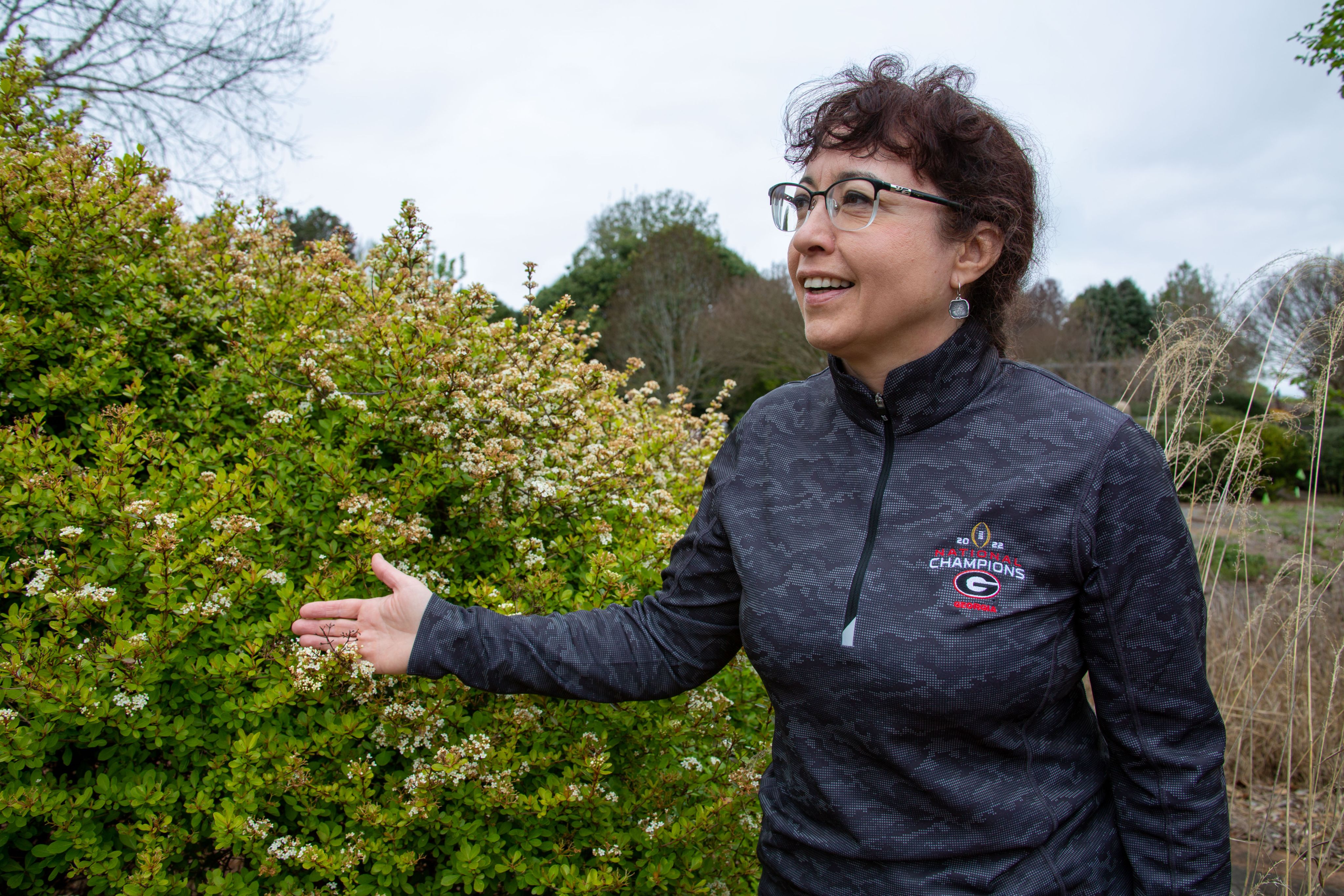 Bodie Pennisi is wearing a black, long sleeved shirt and standing in front of a green shrub. She is smiling as she talks on a somewhat grey, cloudy day.