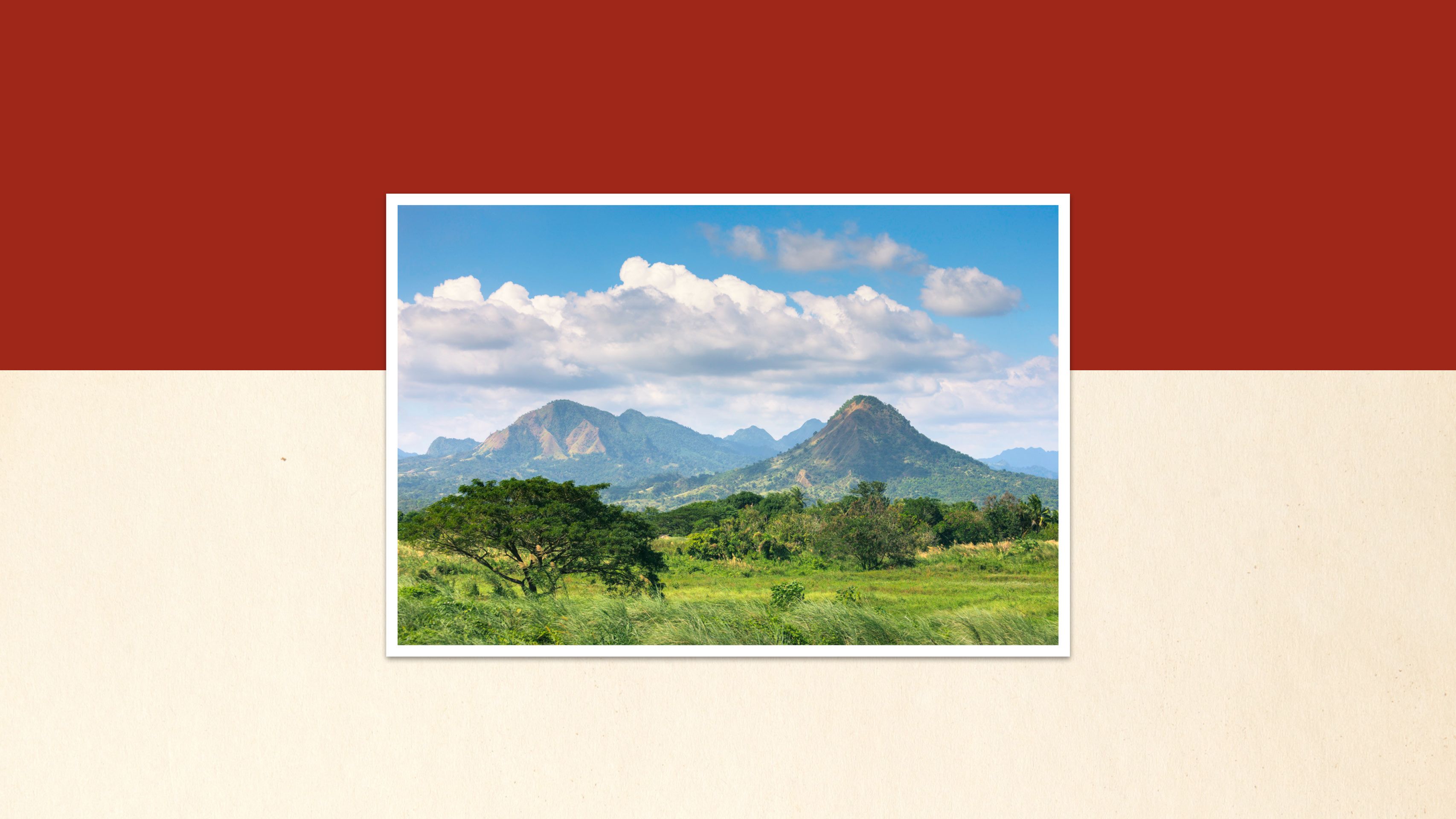 Rolling hills blanketed in lush greenery stretch towards a dramatic mountain range under a vibrant blue sky.