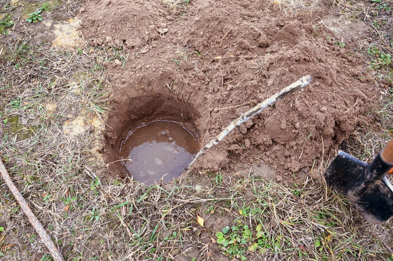 A circular hole dug into soil is filled with standing water.