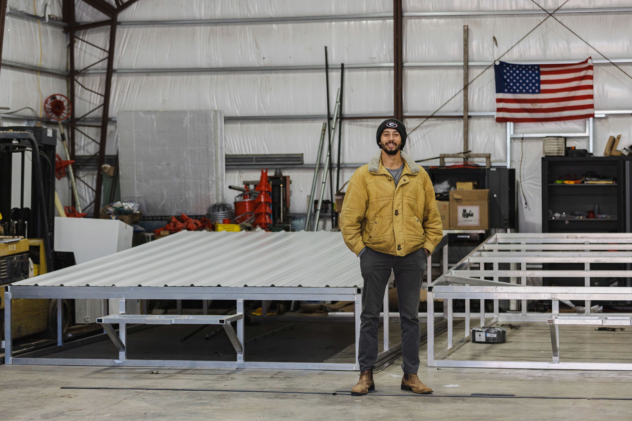 A man in a UGA beanie and tan jacket standing in a warehouse with his hands in his pants pocket.