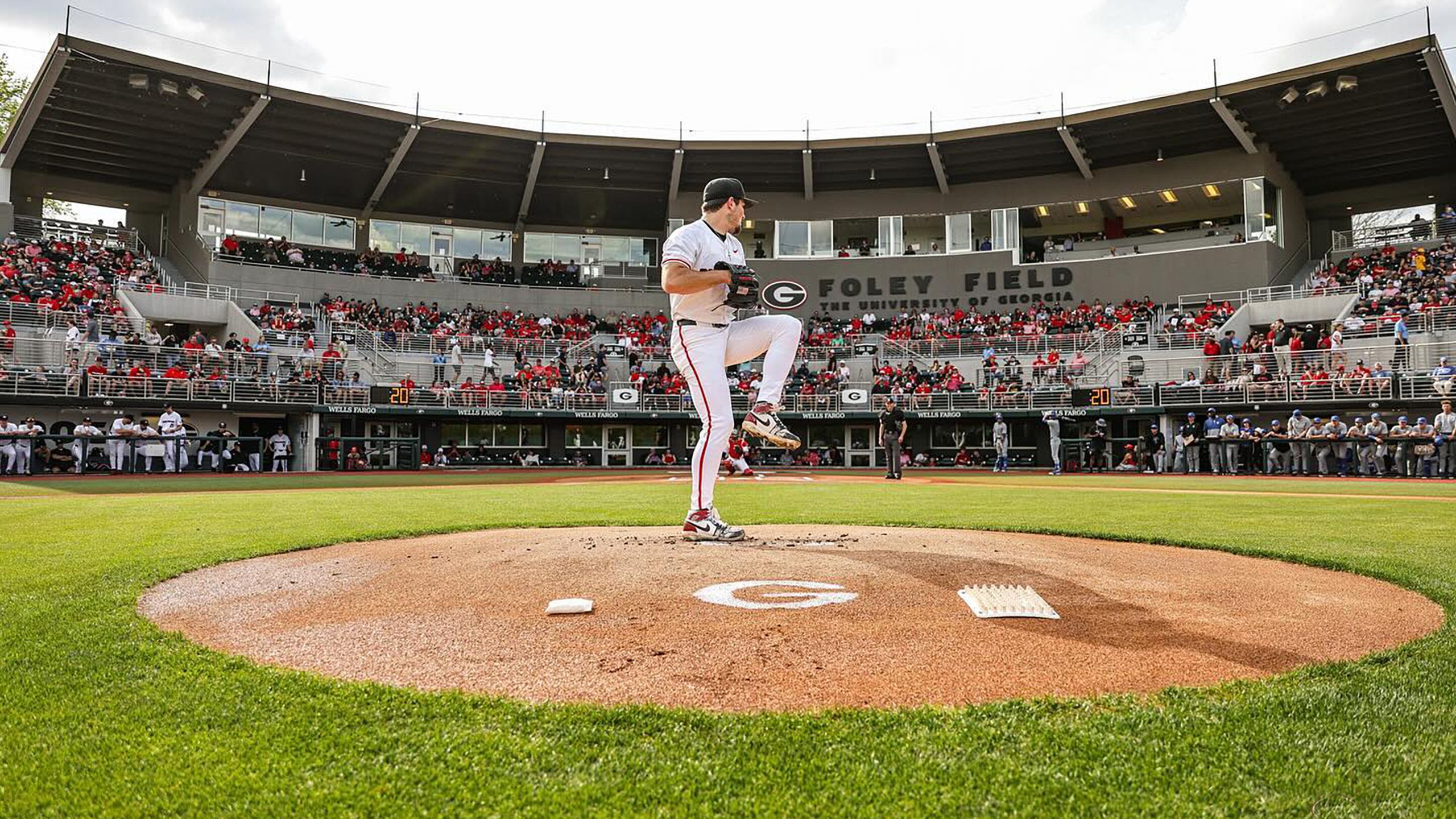 A pitcher standing on the pitcher's mound with his left leg raised about to throw a pitch. The bleachers behind him are filled with people watching the game.