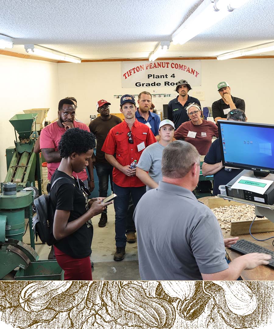 A group of observers watch an employee at Tifton Peanut Company inspect peanuts for quality.