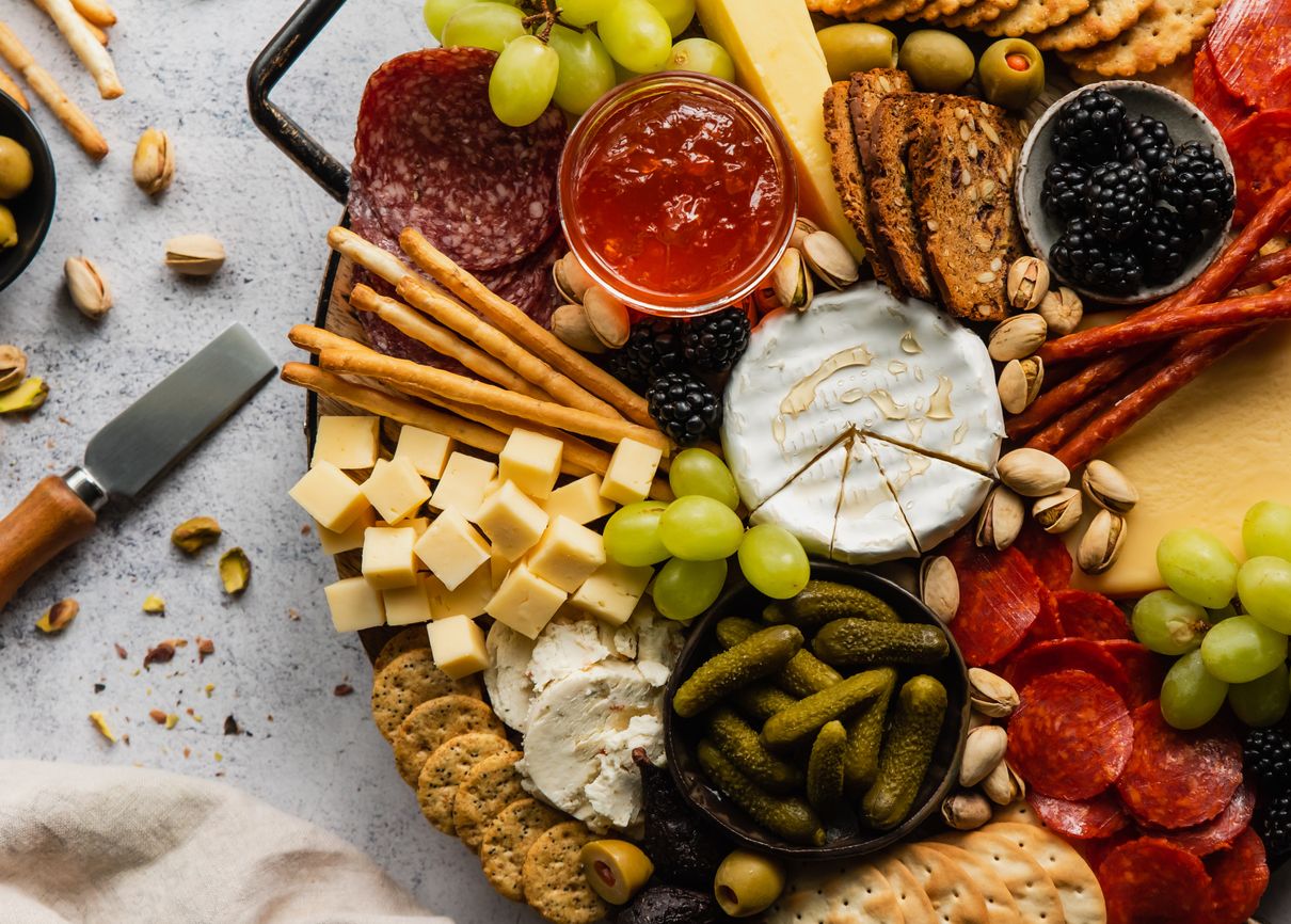 Charcuterie board with cheese, grapes, meat, fruit and jelly next to a spreading knife and pistachios