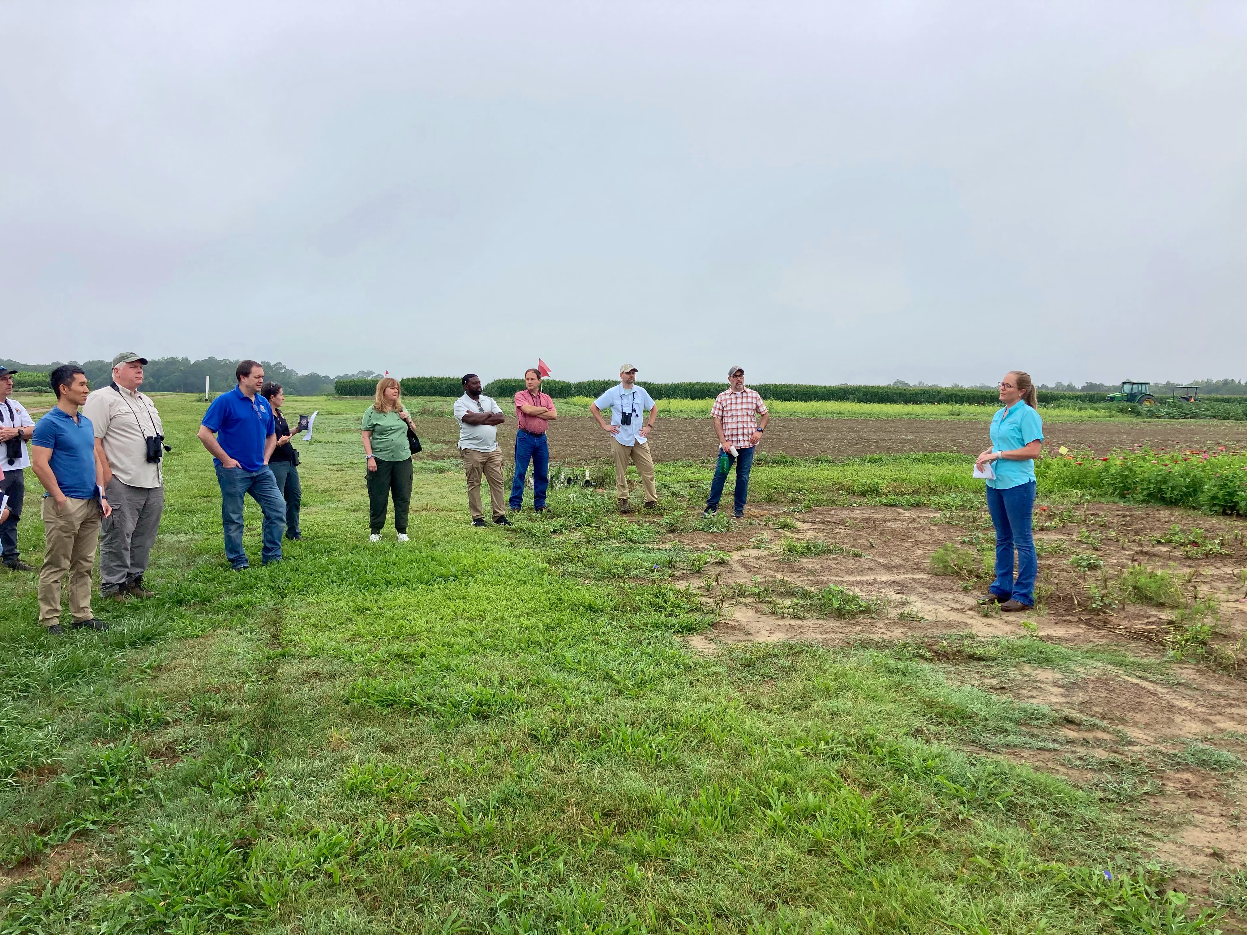 A group of people stand in a field while listening to Randell-Singleton during a workshop. Randell-Singleton (far right) wears a blue shirt and bluejeans. 