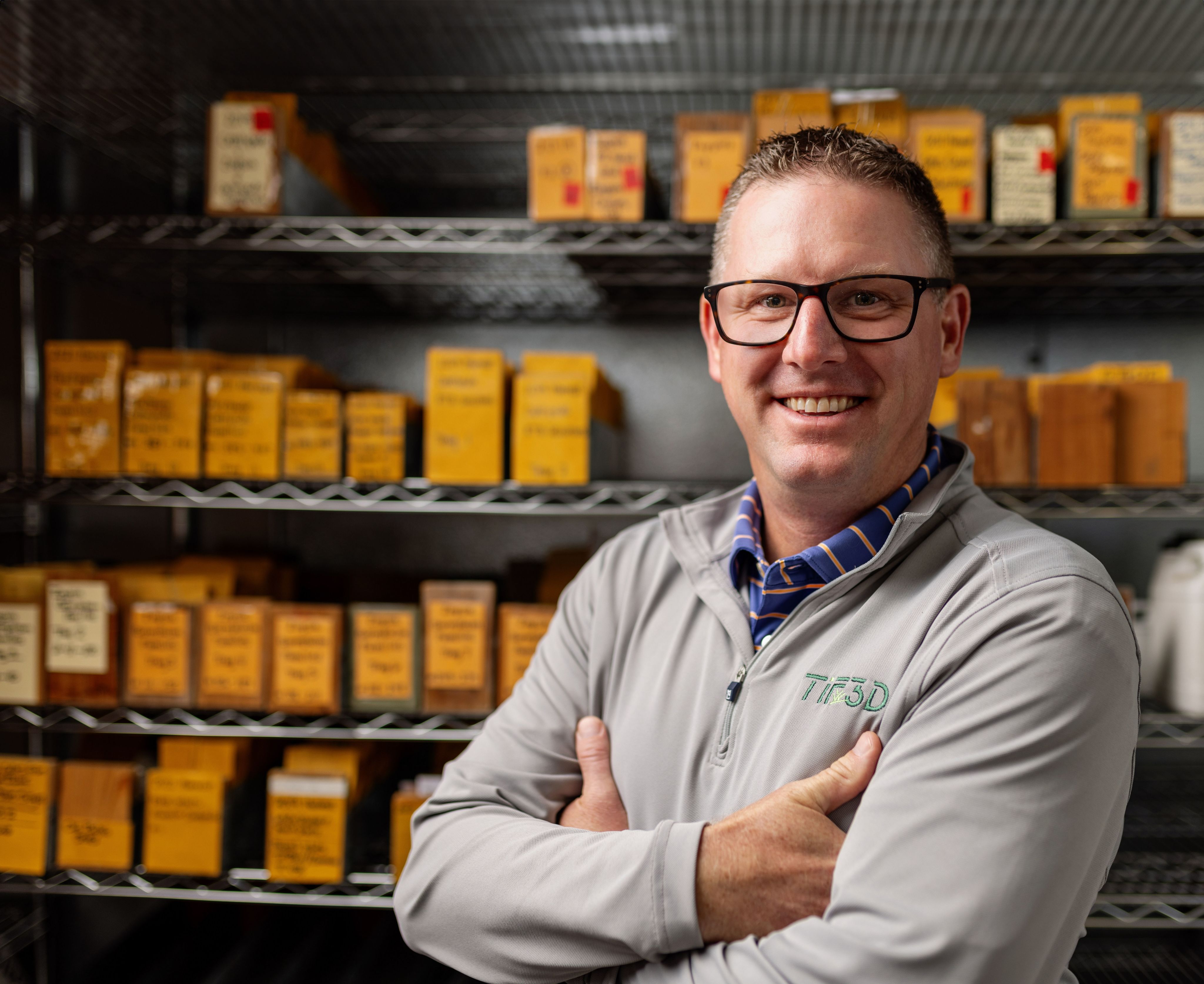 A headshot of Schwartz, who's wearing glasses, while standing in the storage room where shelves of grass seeds are lined up.