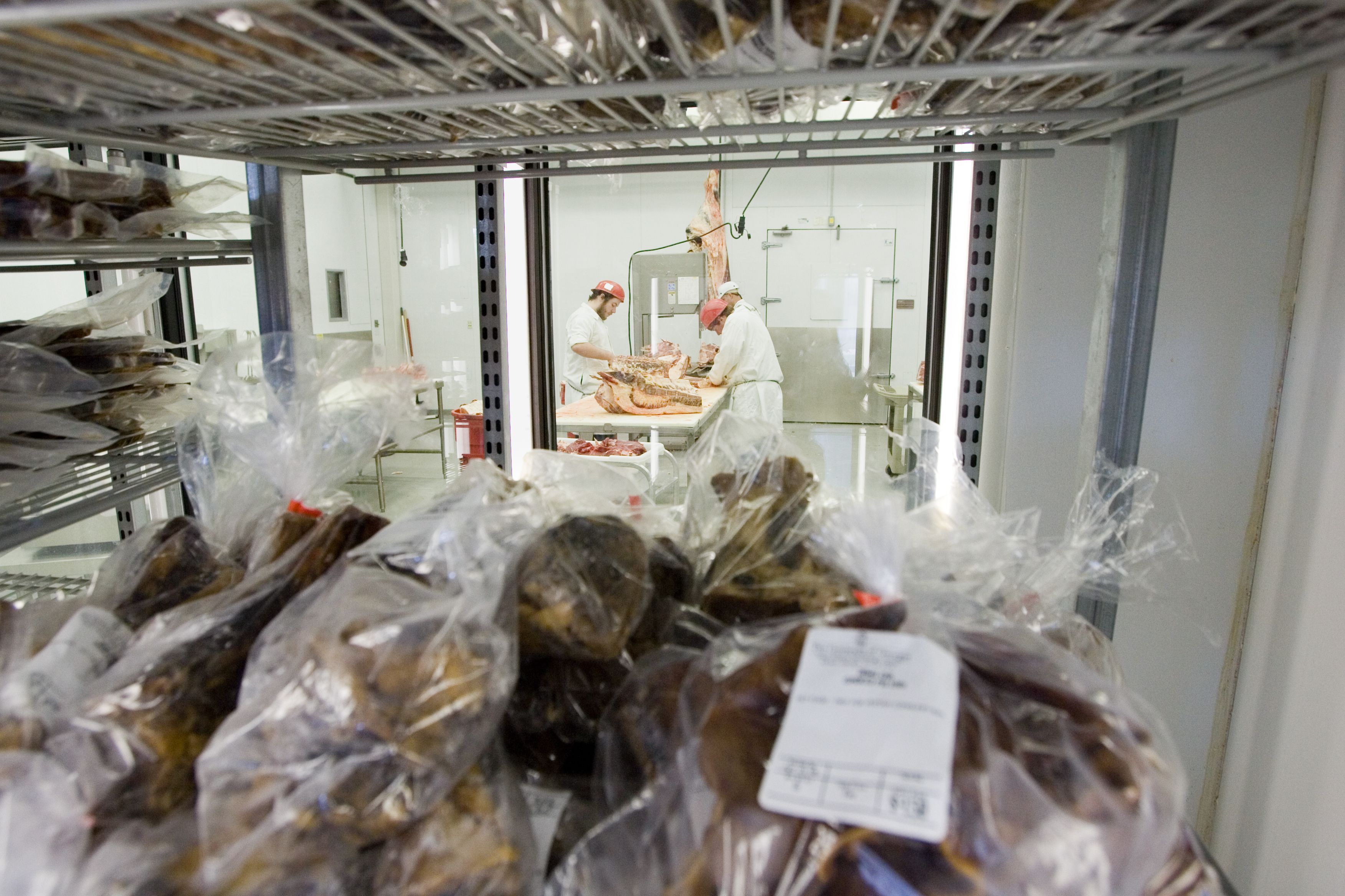 Looking through a freezer full of packaged meat into a meat cutting room.