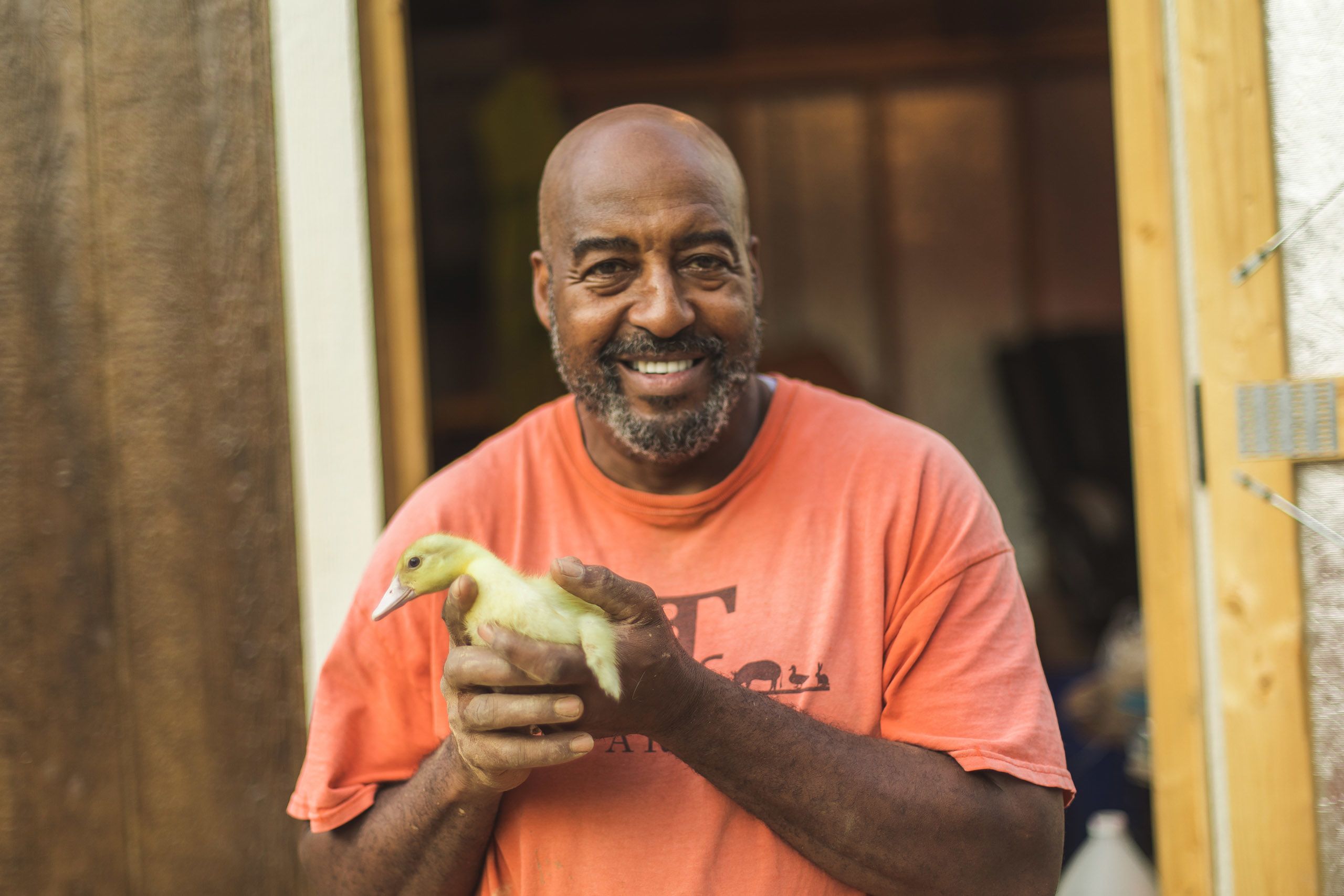 Iteago Felton is in an orange t-shirt, holding a baby duck and smiling at the camera.