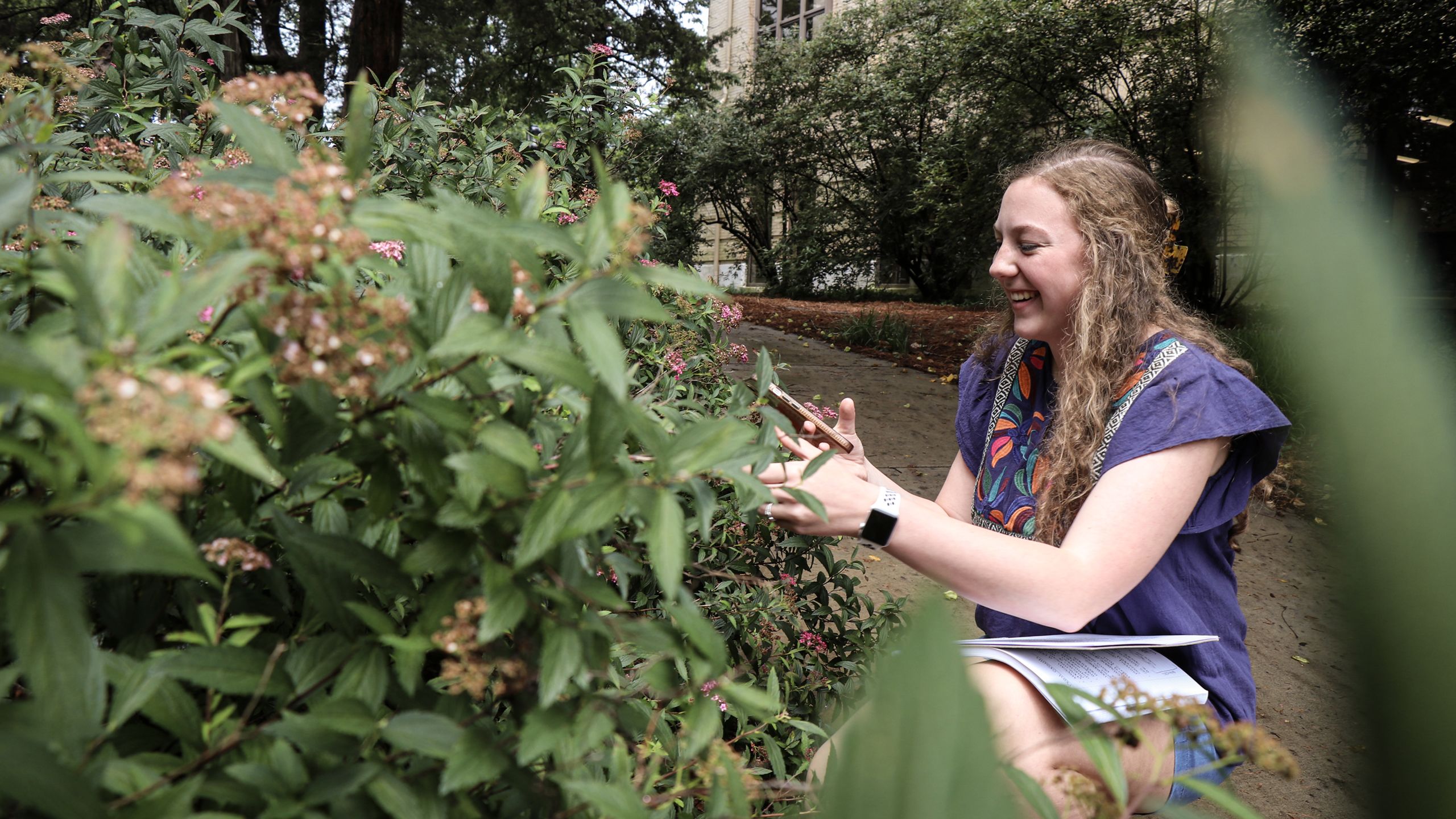 Molly Greer crouches next to a Japanese Spirea bush.