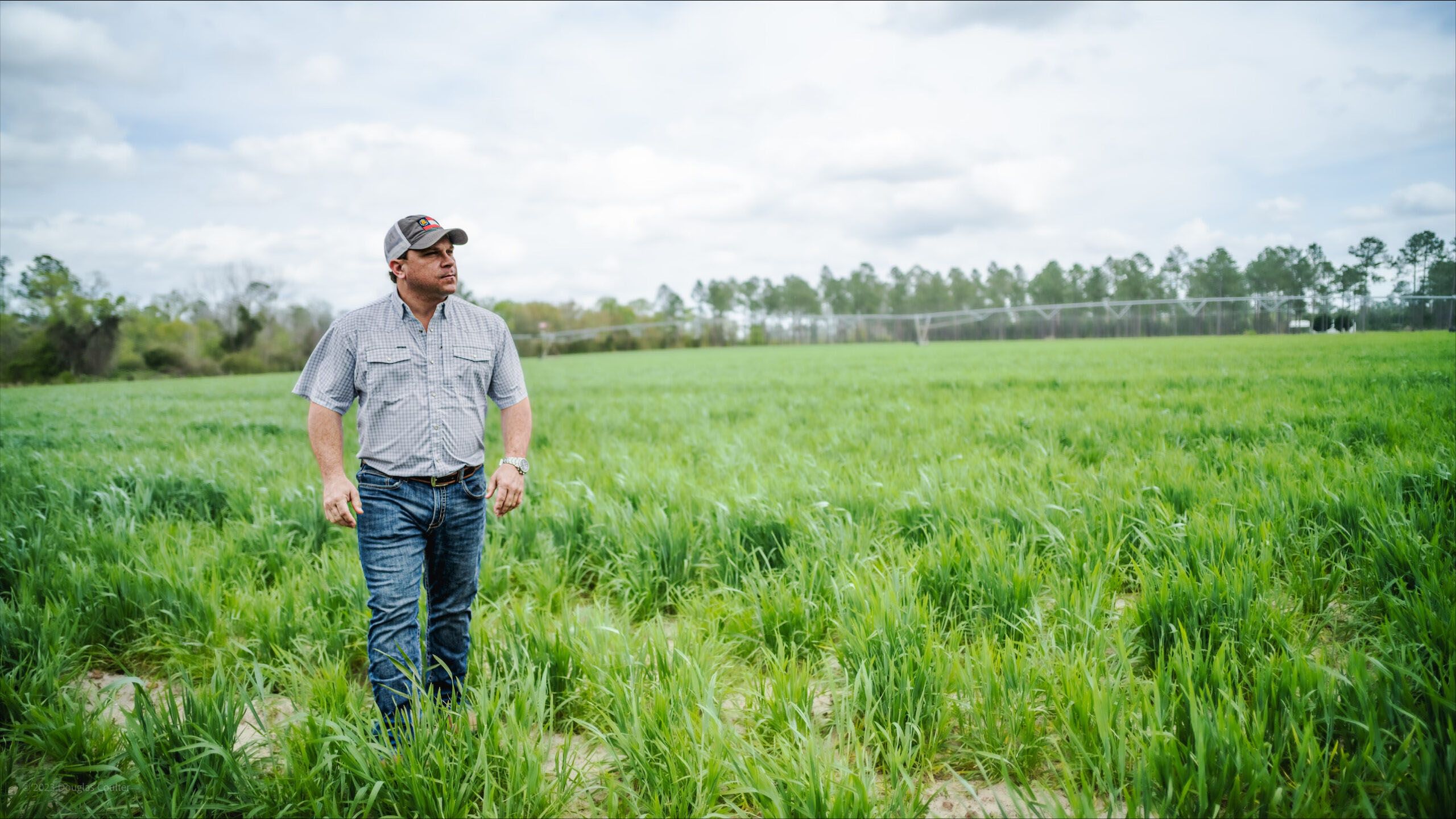 Tyler Harper walks through a grassy field wearing work clothes.