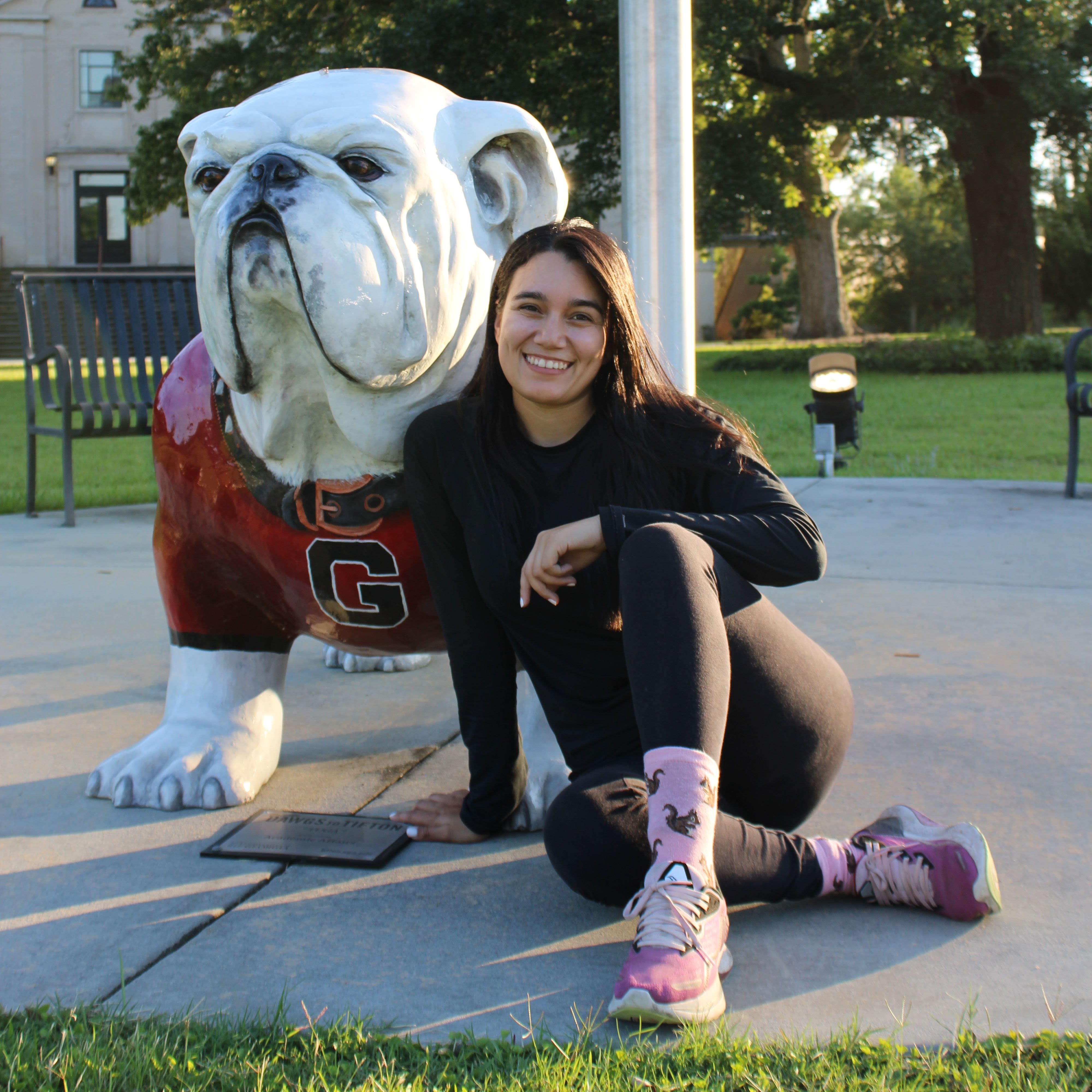 Lilian Carcamo, dressed in all black with pink socks and shoes, sits in front of a Georgia bulldog statue. 