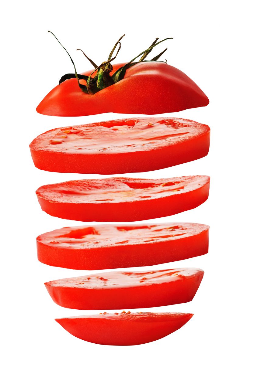 Image of a tomato sliced into several pieces and suspended in air with a white background.