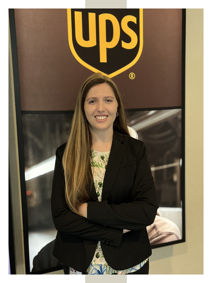 Wearing a blouse and blazer, Samantha Siragusa poses in front of a UPS logo at work