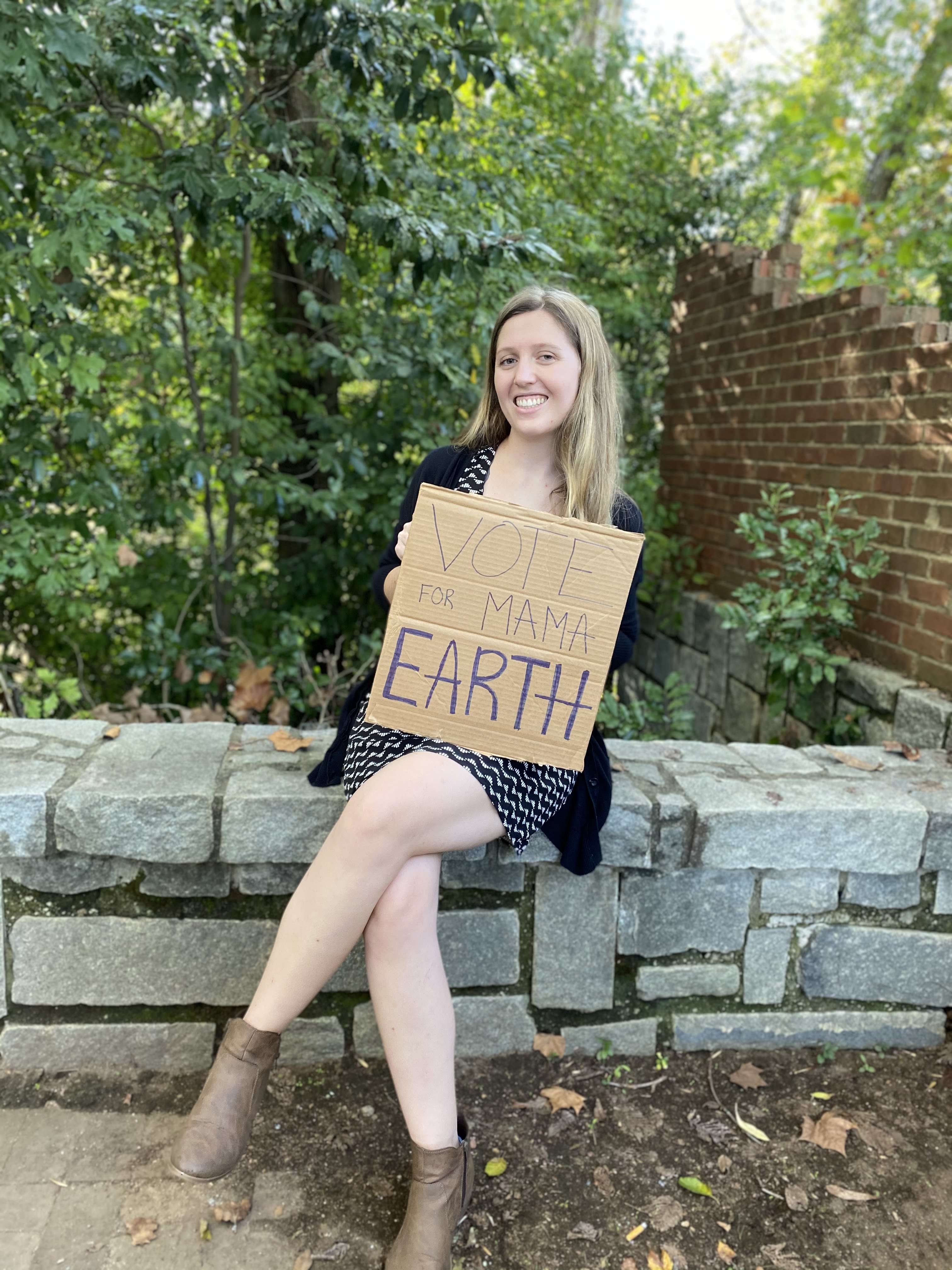 Samantha Siragusa smiles while holding a cardboard sign that says "Vote for Mama Earth"