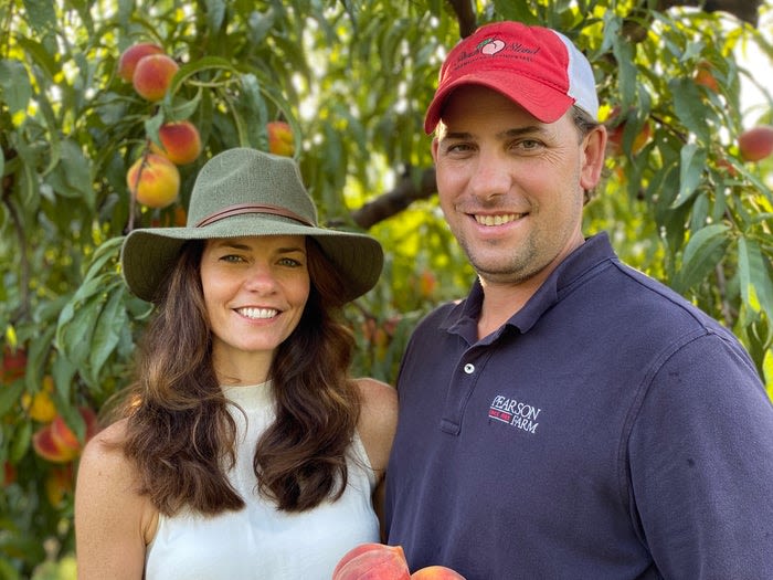 Man and a woman stand in front a peach tree