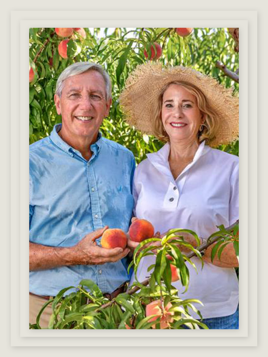 A man and a woman in an excellent straw hat hold peaches