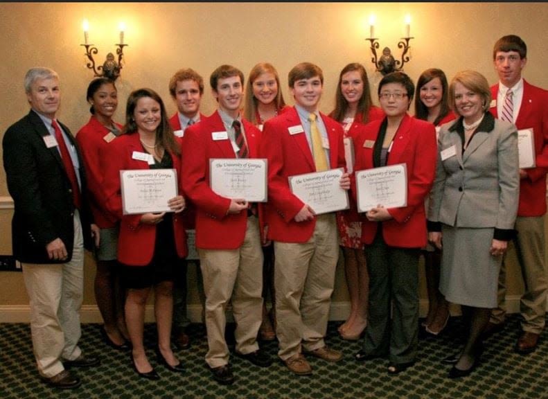Ten student ambassadors wearing red blazers pose for a photo holding certificates