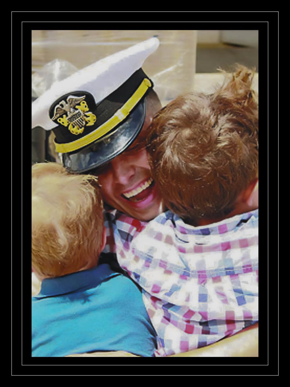 Man in white Navy service dress smiles broadly while hugging his two boys