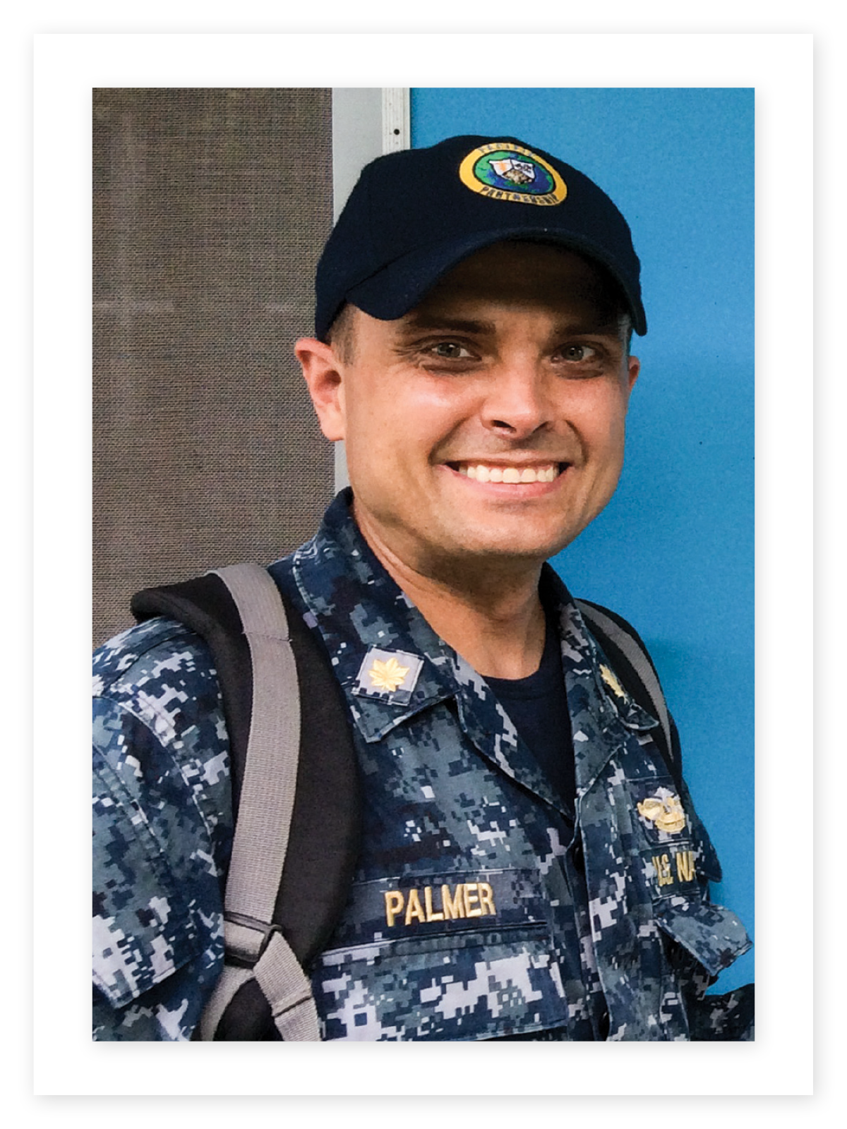 Toby Palmer smiles in blue camouflage Navy uniform and emblazoned dark baseball cap