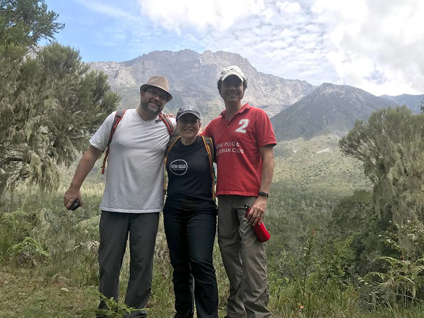 Three travelers smiling with a mountain landscape behind them.