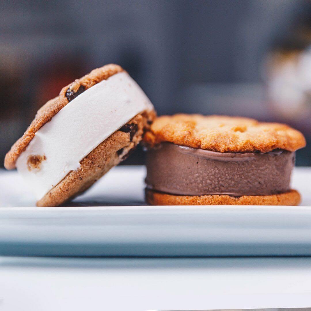 Two ice cream sandwiches made of chocolate chip cookies, with one filled with vanilla ice cream and the other chocolate.