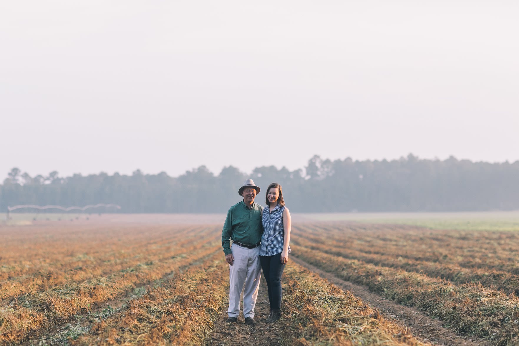 Father and adult daughter in a plowed peanut field.