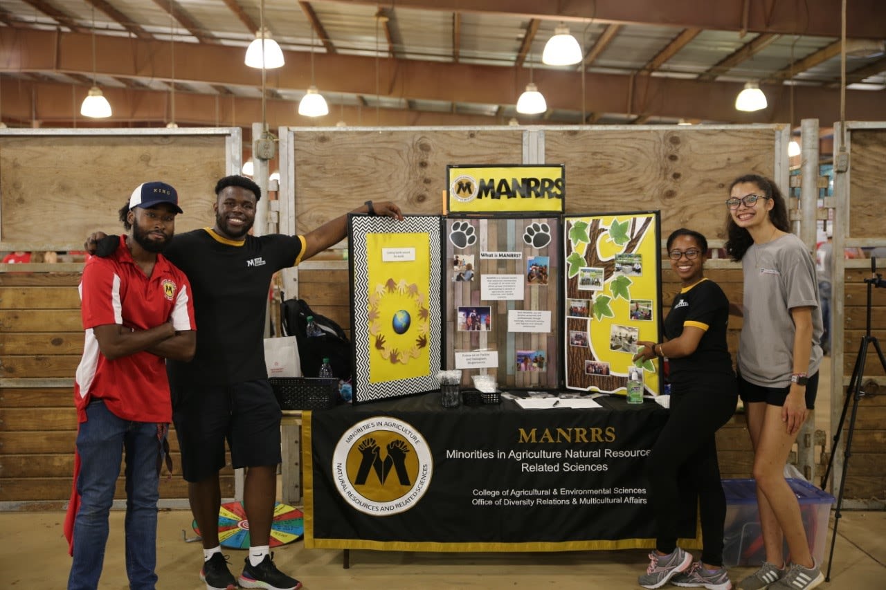 Four students pose with MANNRS display at a student event