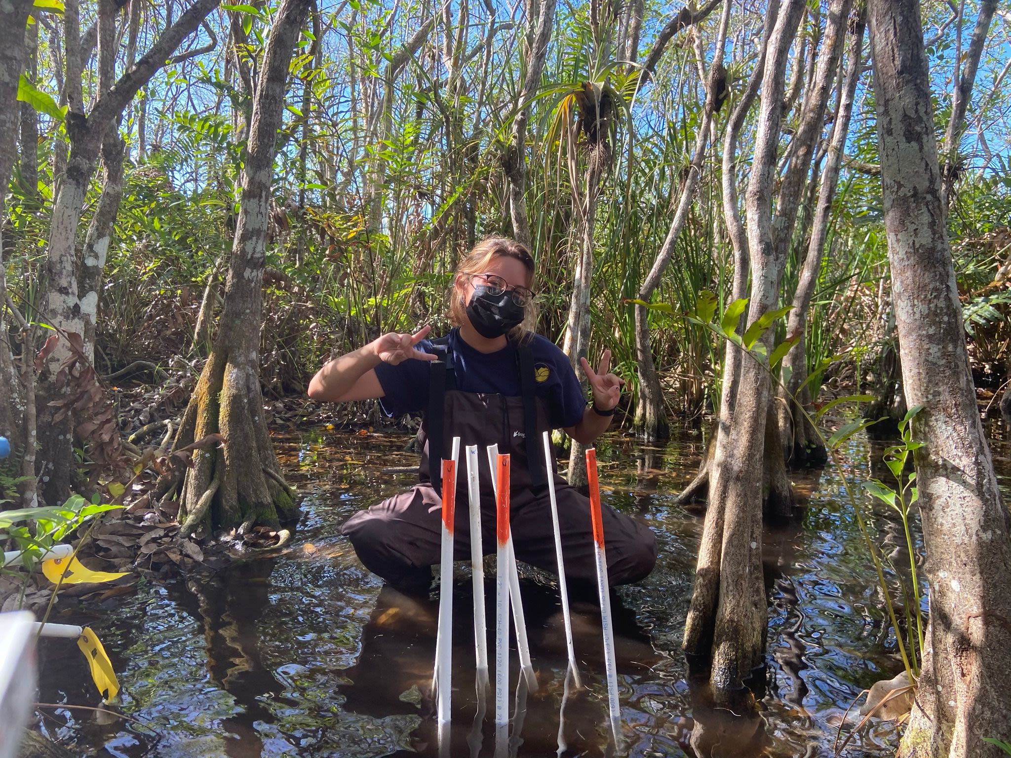Lugo-Arroyo does fieldwork, taking samples from water while wearing a mask and flashing peace signs.