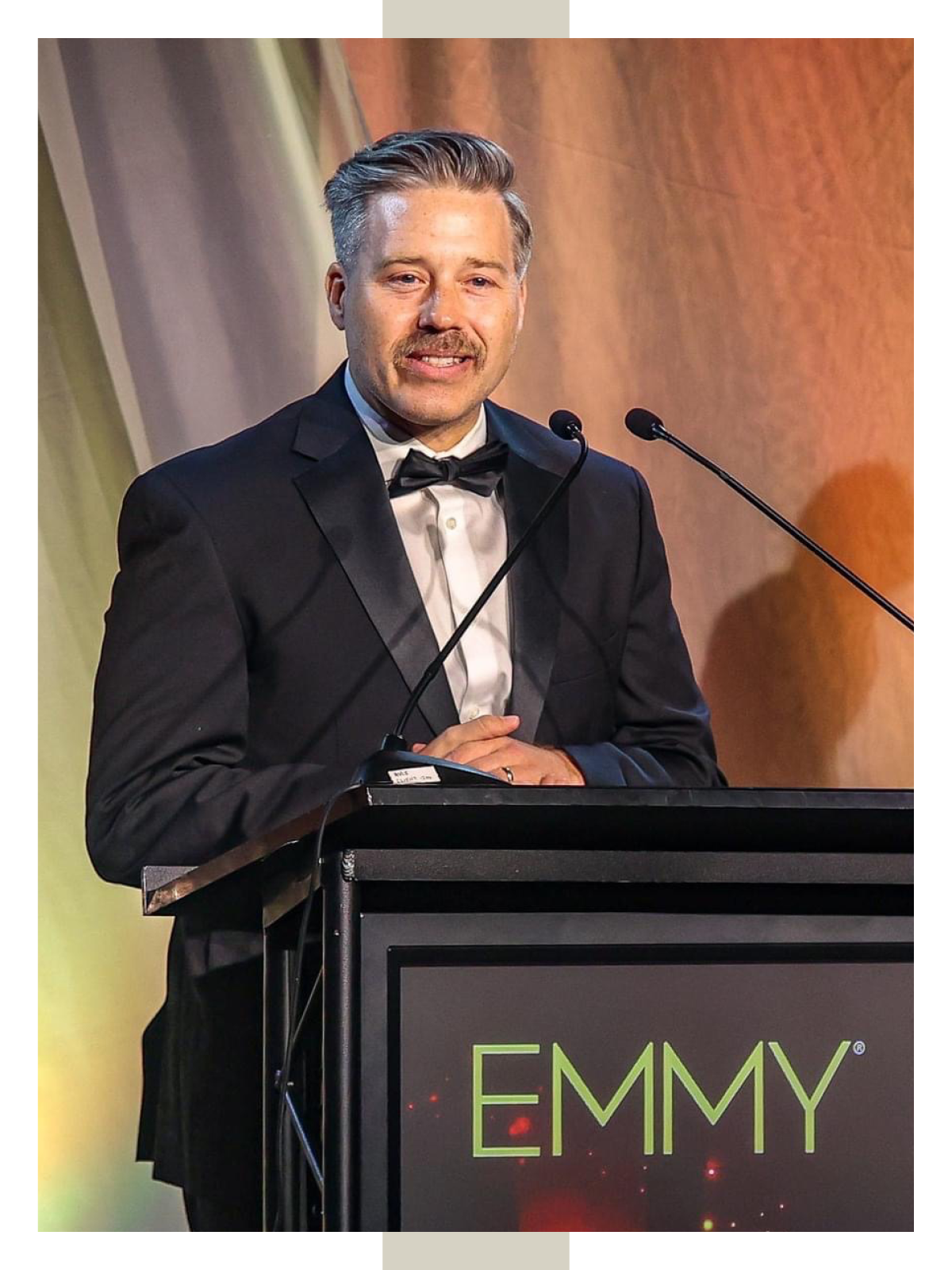 Man in tuxedo stands at a lectern marked "Emmy"