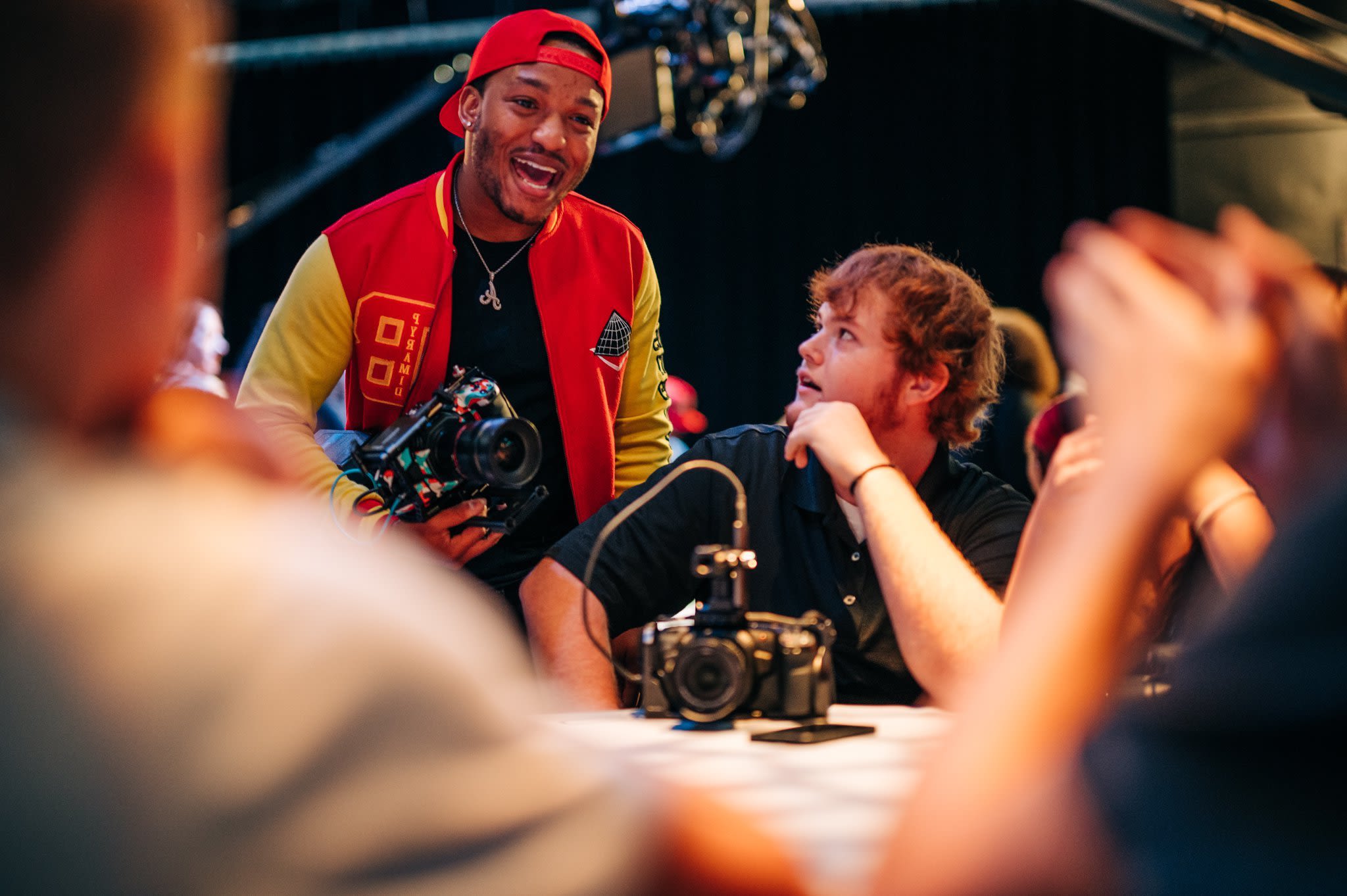 Rapper and Brand Ambassador Nosakhere Andrews (Mr. 2-17) talks to a table full of attendees at the GPB event while holding a camera and wearing a Hope Givers hat