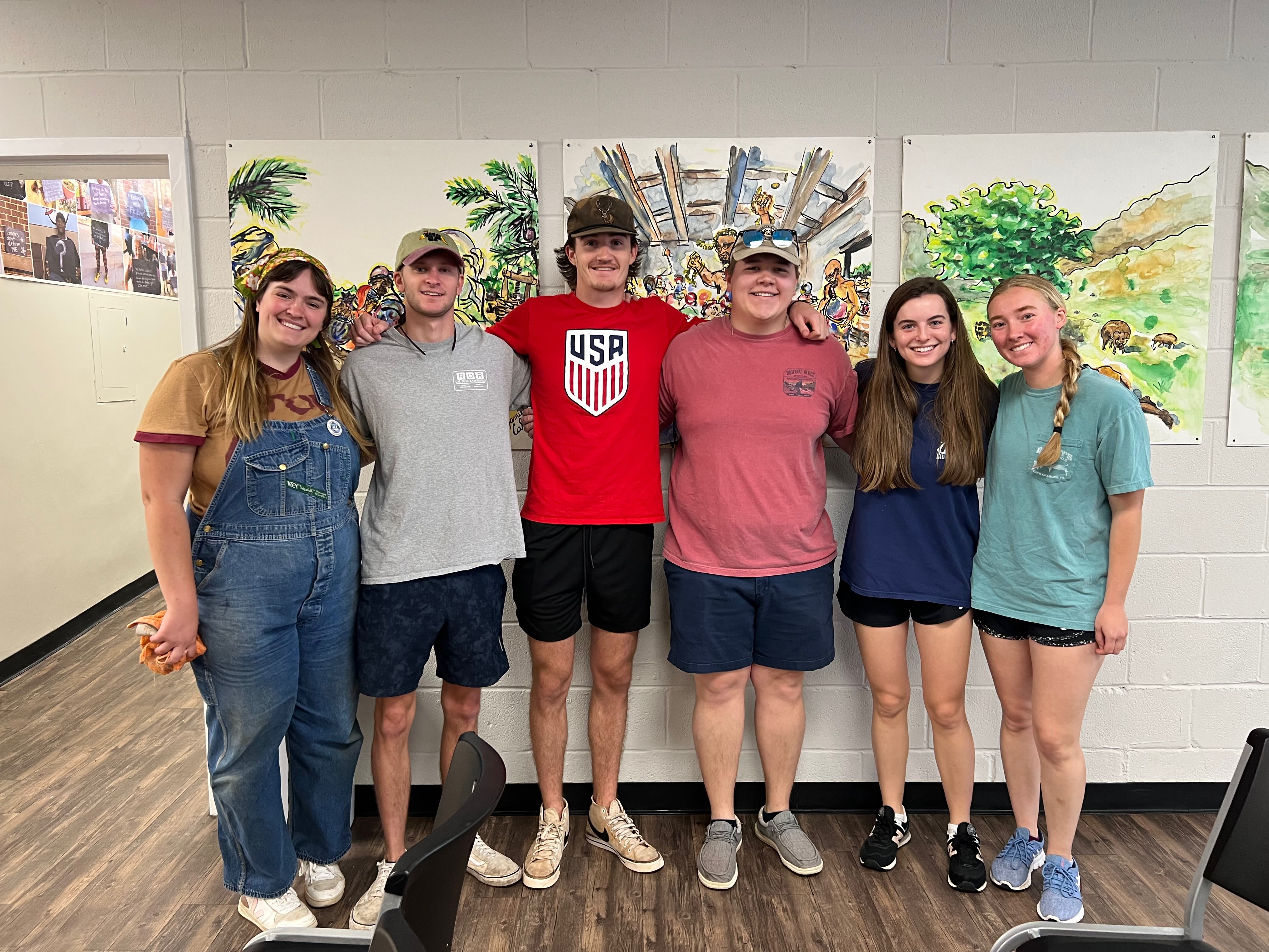 Six students gather together in front of painted art panels in a hallway